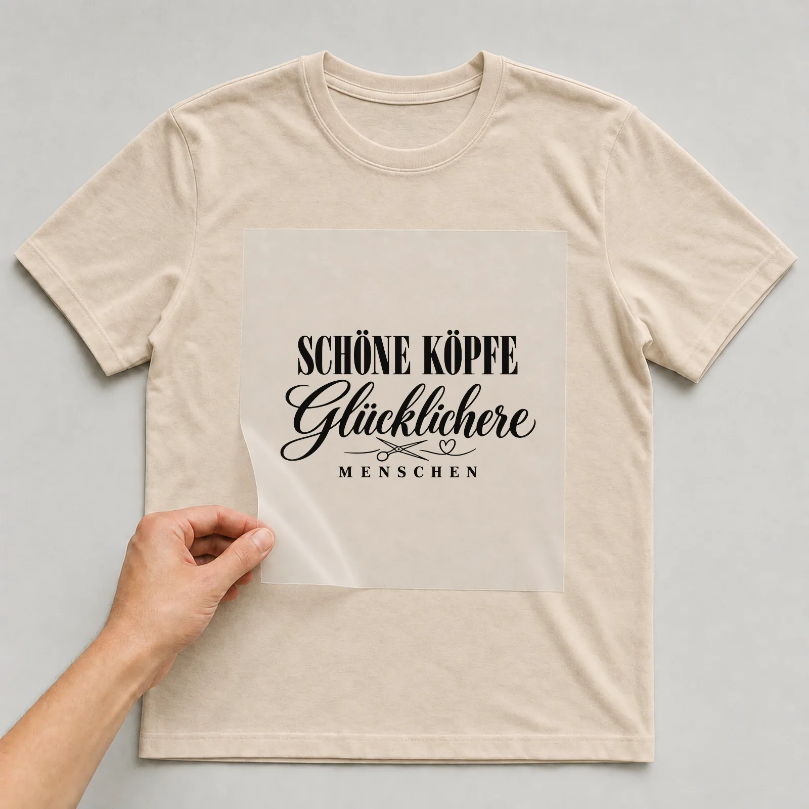 Bügelbild „Schöne Köpfe glücklichere Menschen“ auf beigem T-Shirt, Folie wird aufgelegt