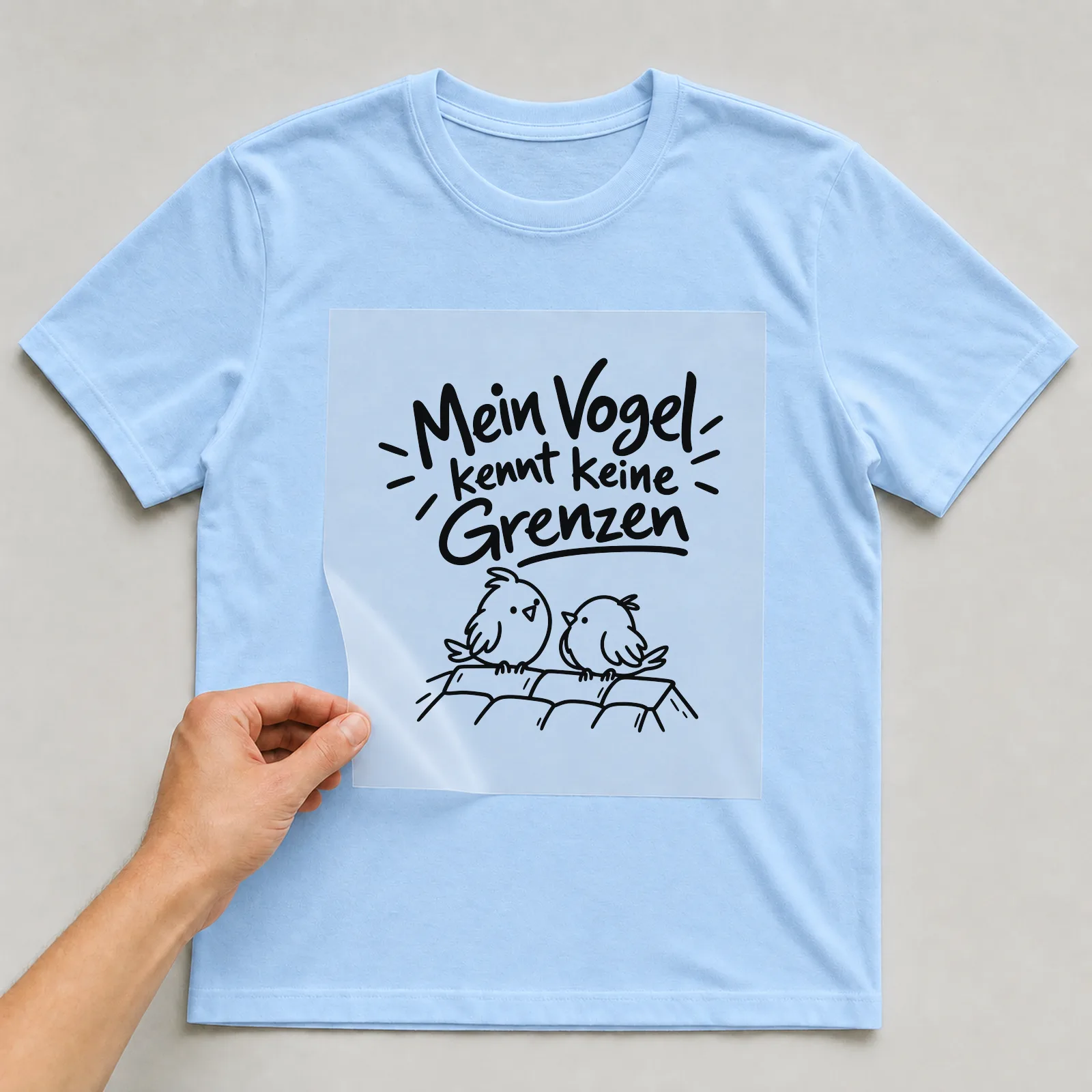 Bügelbild „Mein Vogel kennt keine Grenzen“ auf hellblauem T-Shirt, Folie wird aufgelegt