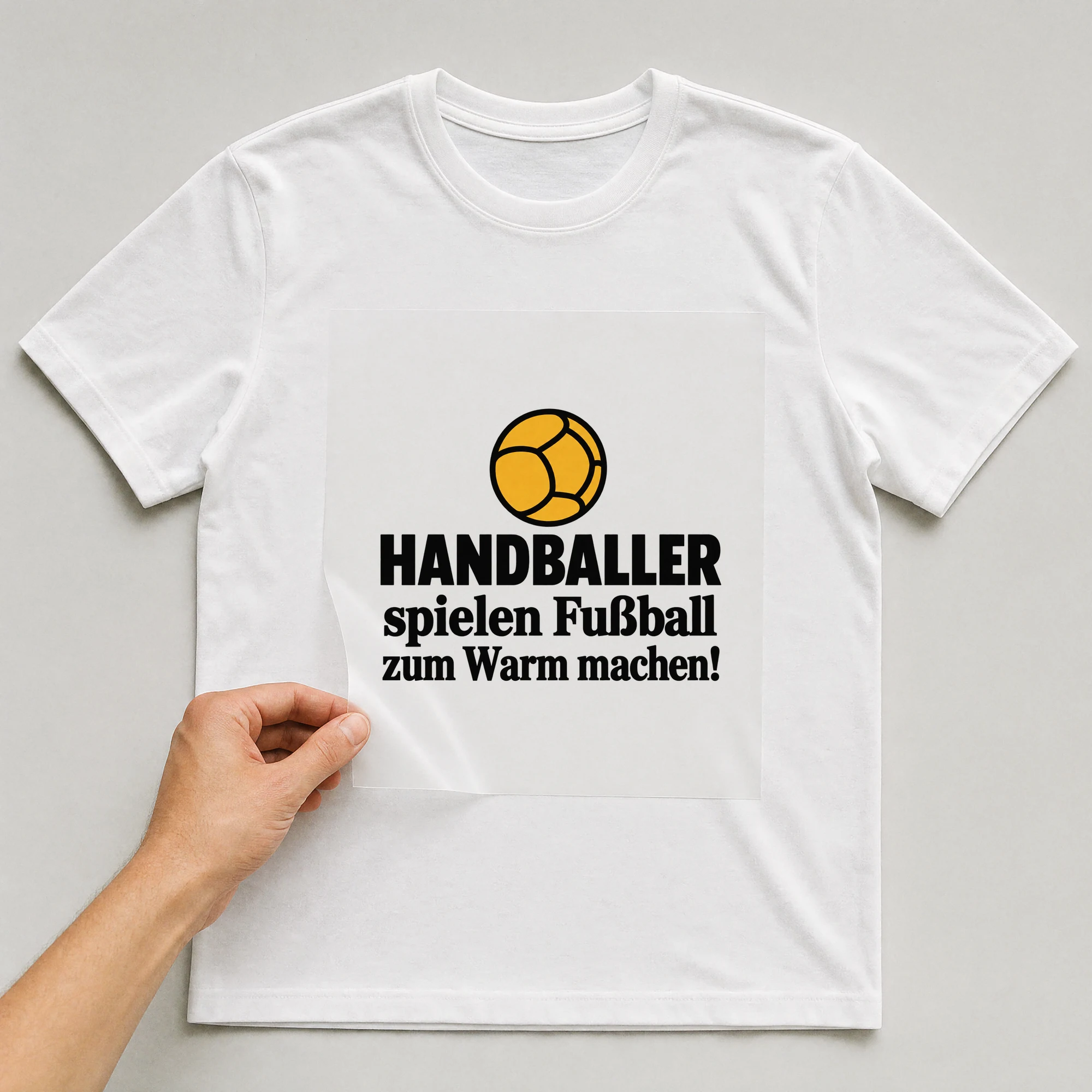 Bügelbild „HANDBALLER spielen Fußball zum Warm machen!“ auf weißem T-Shirt, Folie wird aufgelegt