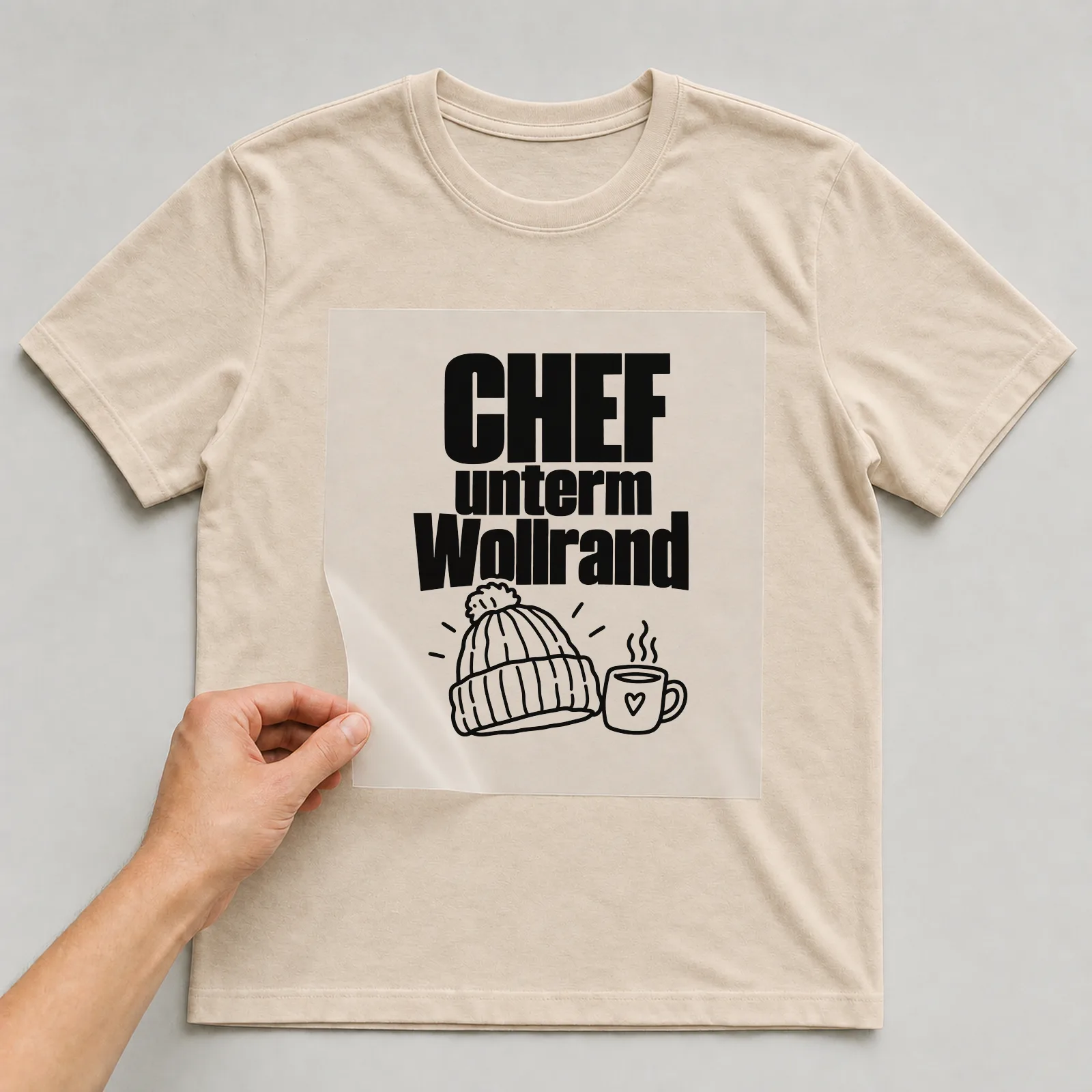 Bügelbild „Chef unterm Wollrand“ auf beigem T-Shirt, Folie wird aufgelegt