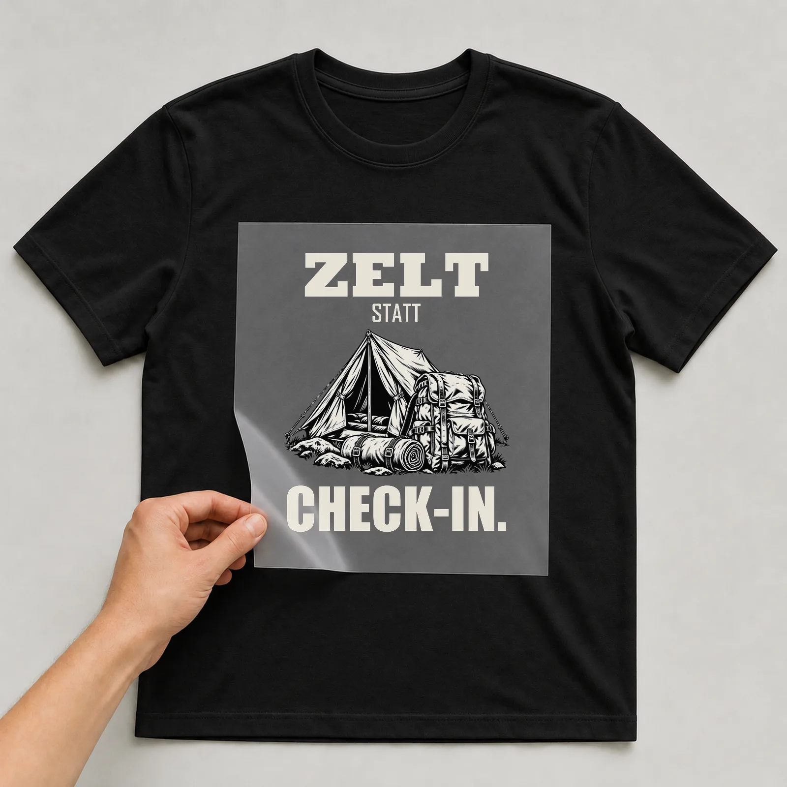 Bügelbild „Zelt statt Check-in“ auf schwarzem T-Shirt, Folie wird aufgelegt
