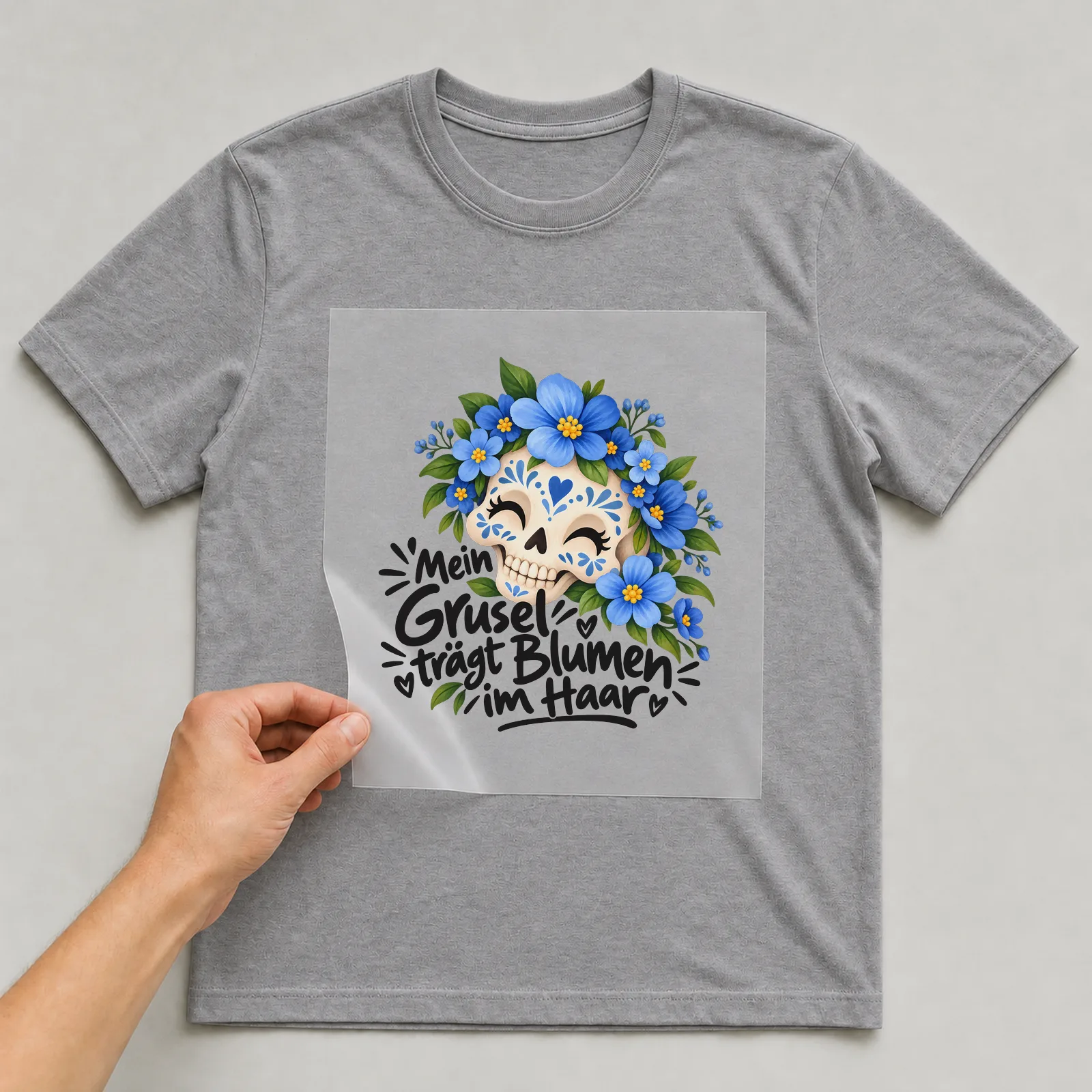 Bügelbild „Mein Grusel trägt Blumen im Haar“ auf grauem T-Shirt, Folie wird aufgelegt