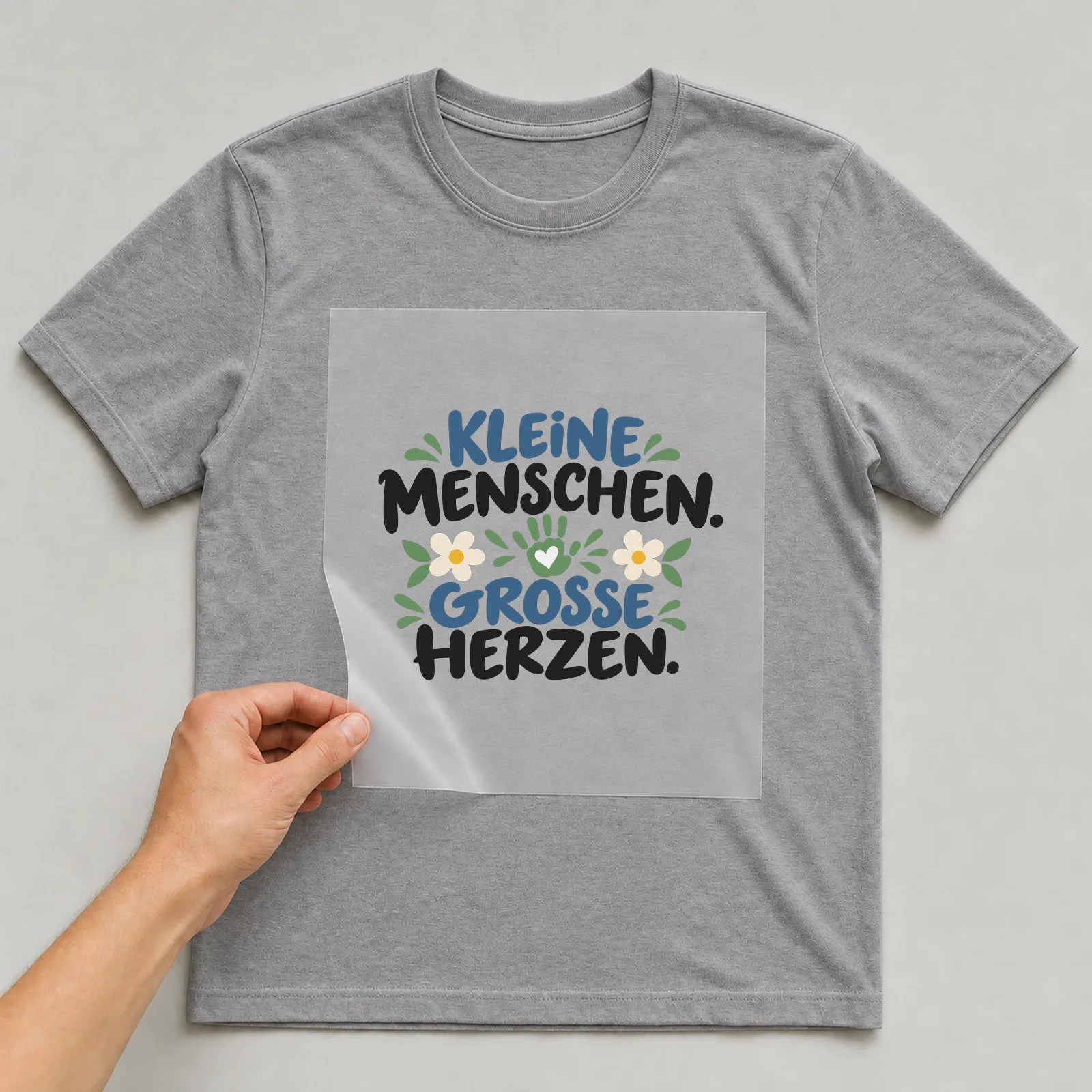 Bügelbild „Kleine Menschen. Große herzen.“ auf grauem T-Shirt, Folie wird aufgelegt