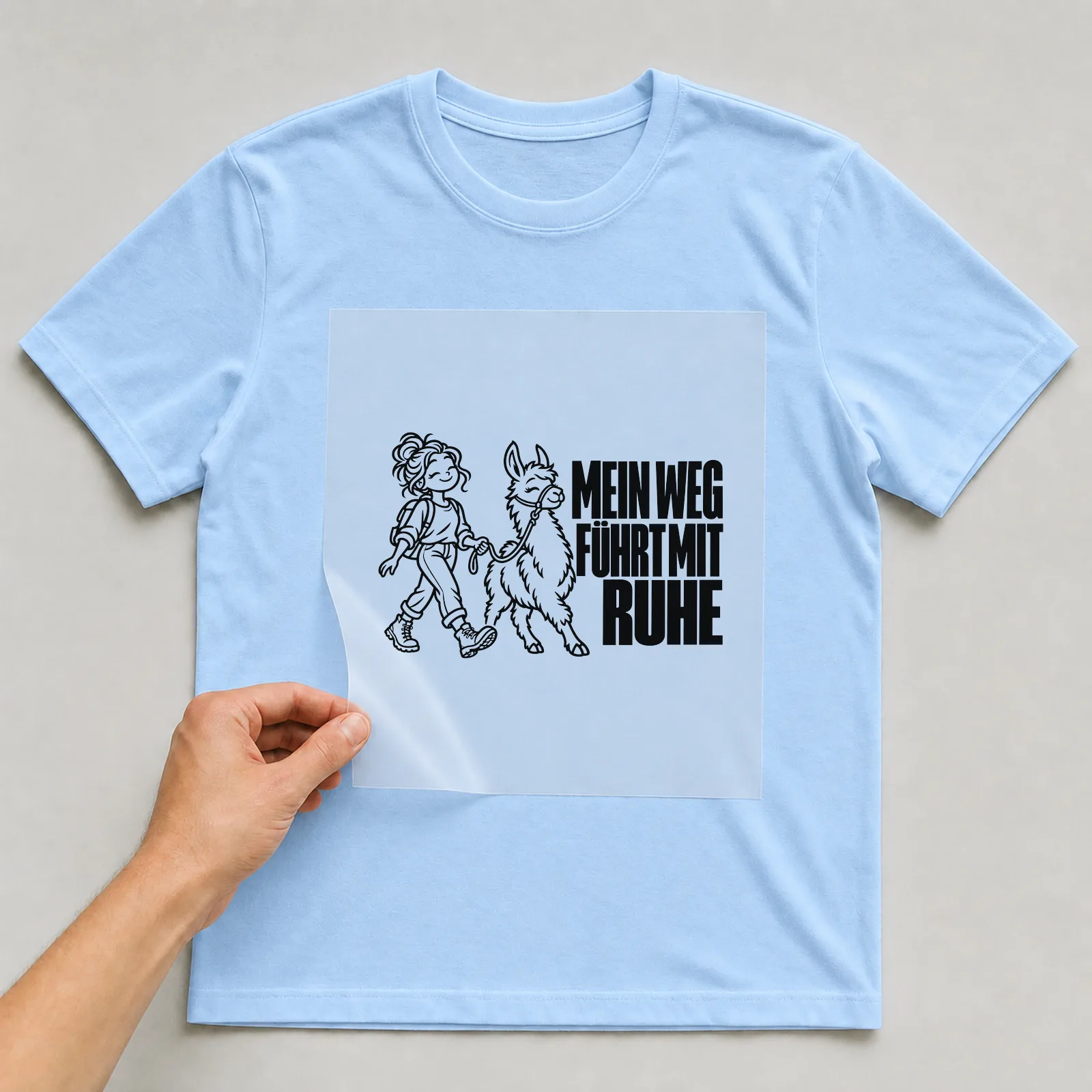 Bügelbild „Mein weg führt mit Ruhe“ auf hellblauem T-Shirt, Folie wird aufgelegt