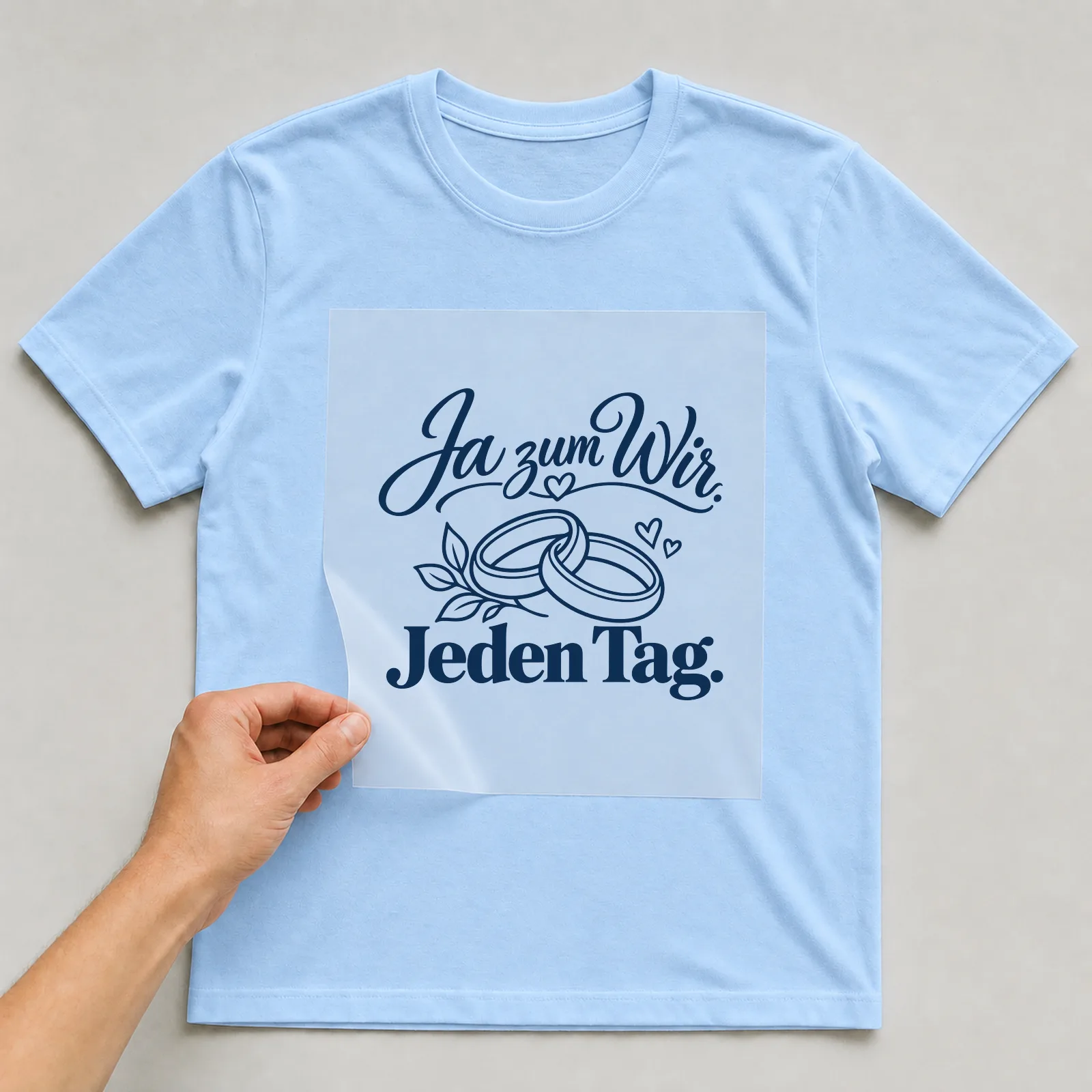 Bügelbild „Ja zum Wir. Jeden Tag.“ auf hellblauem T-Shirt, Folie wird aufgelegt