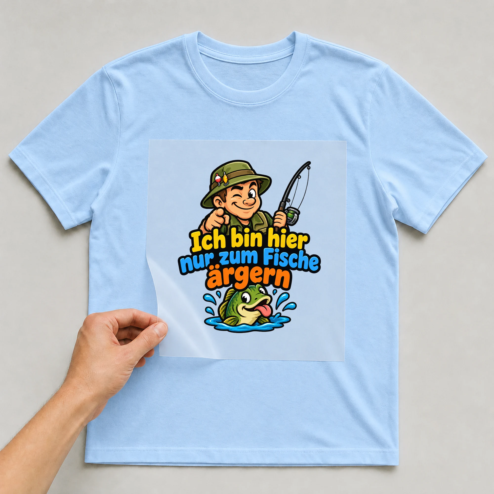 Bügelbild „Ich bin hier nur zum Fische ärgern“ auf babyblauem T-Shirt, Folie wird aufgelegt