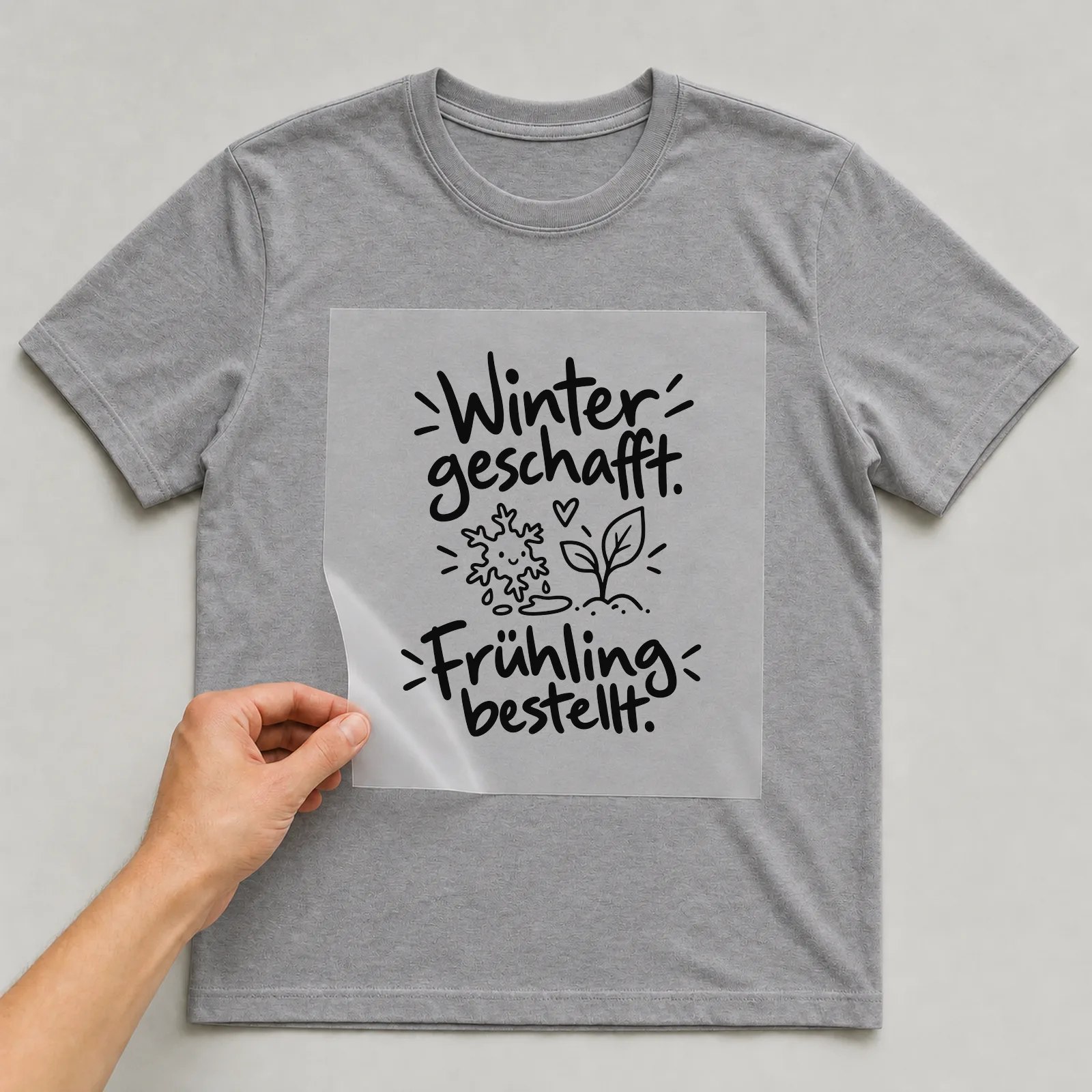 Bügelbild „Winter geschafft. Frühling bestellt.“ auf grauem T-Shirt, Folie wird aufgelegt