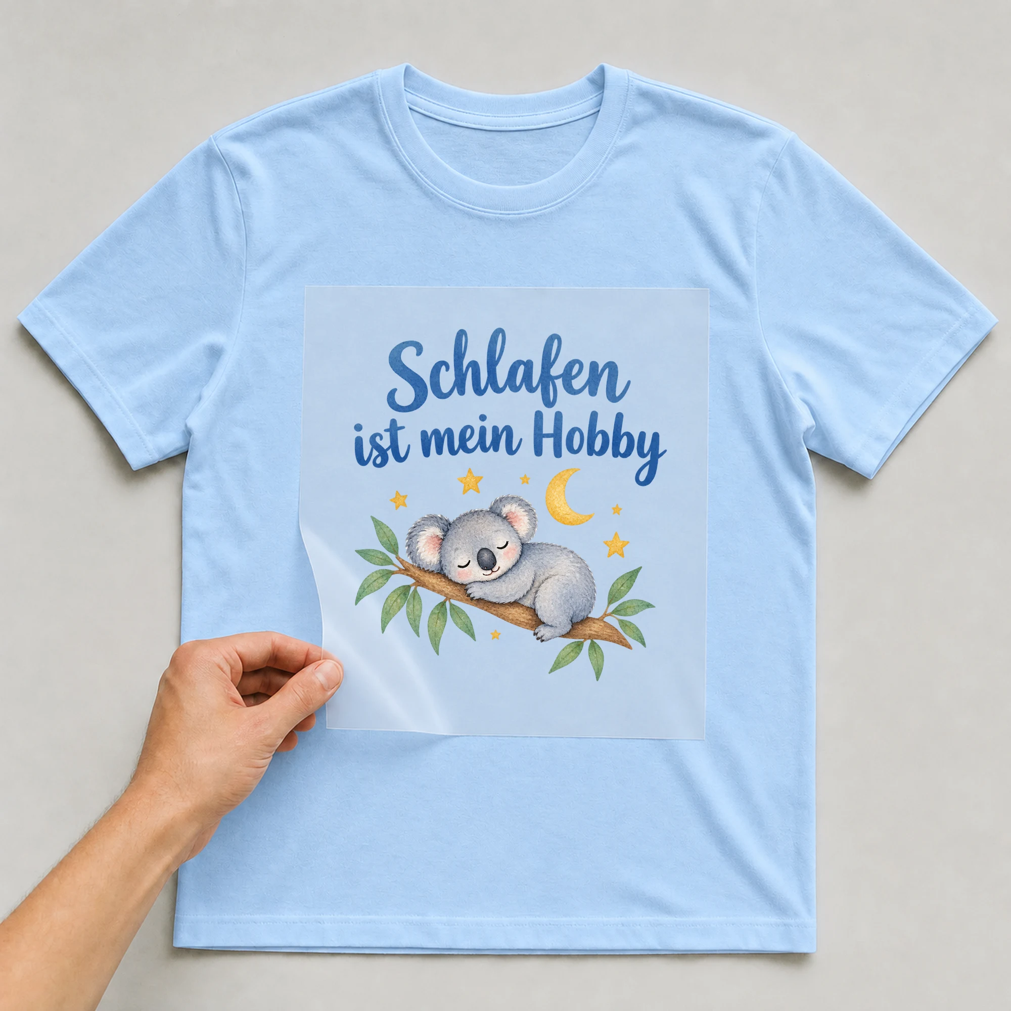 Bügelbild „Schlafen ist mein Hobby“ auf babyblauem T-Shirt, Folie wird aufgelegt