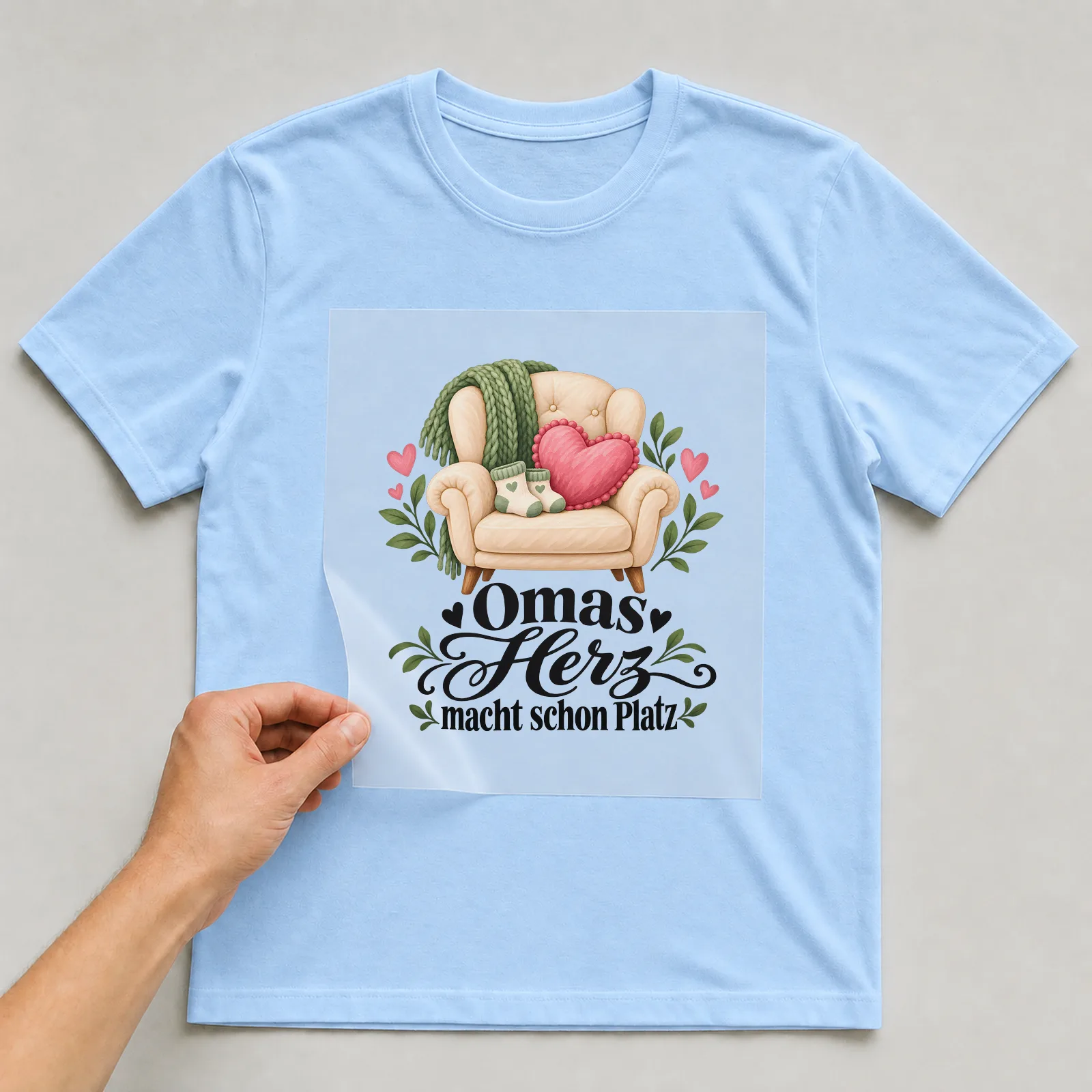 Bügelbild „Omas Herz macht schon Platz“ auf hellblauem T-Shirt, Folie wird aufgelegt