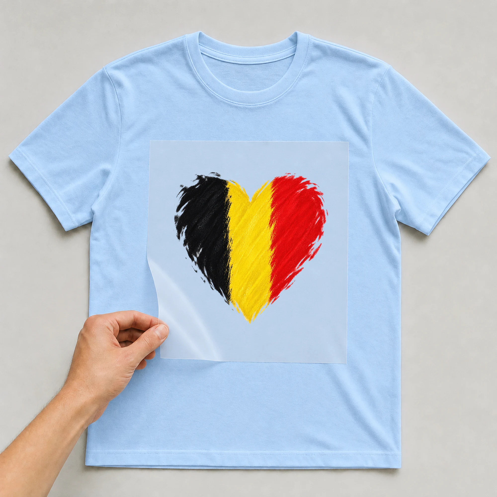 Bügelbild „Herz in Schwarz Gelb Rot“ auf babyblauem T-Shirt, Folie wird aufgelegt