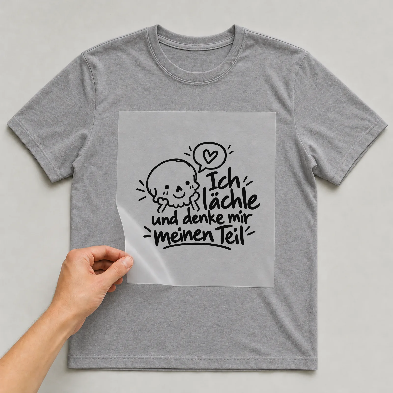 Bügelbild „Ich lächle und denke mir meinen Teil“ auf grauem T-Shirt, Folie wird aufgelegt