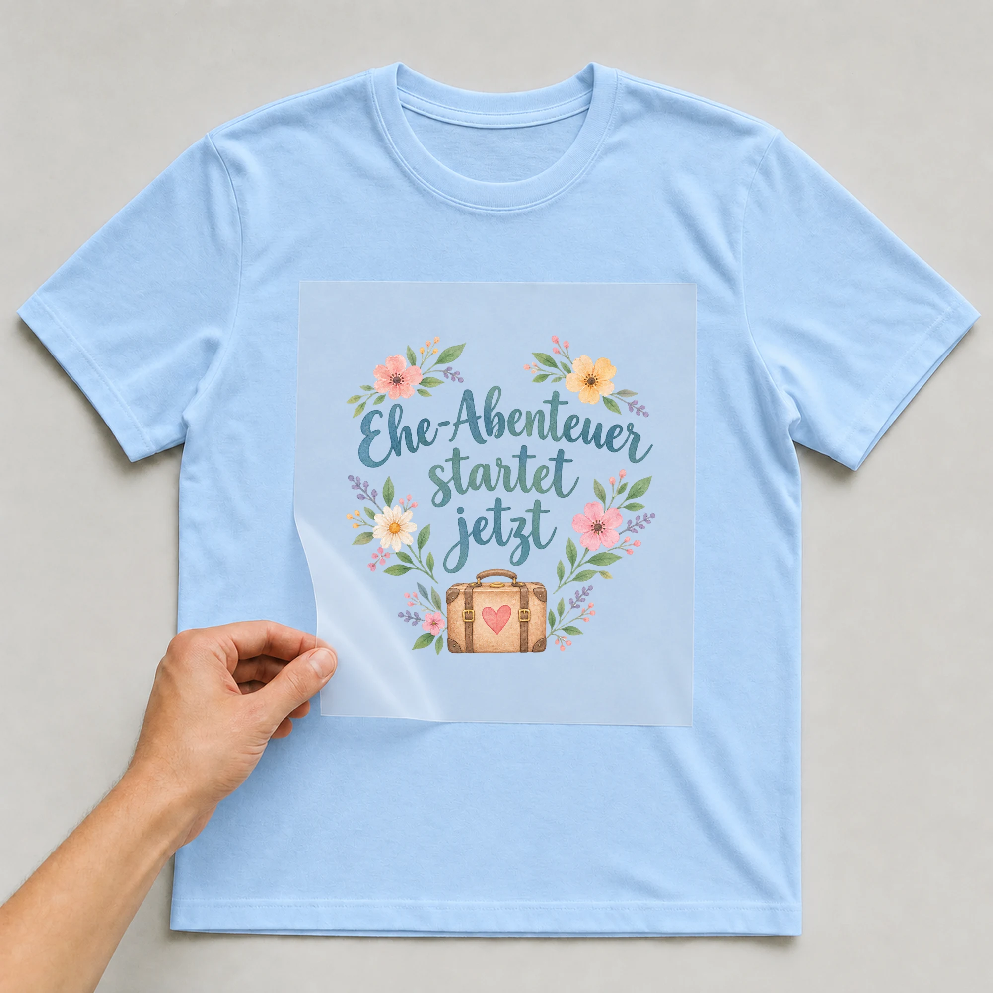 Bügelbild „Ehe abenteuer startet jetzt“ auf babyblauem T-Shirt, Folie wird aufgelegt