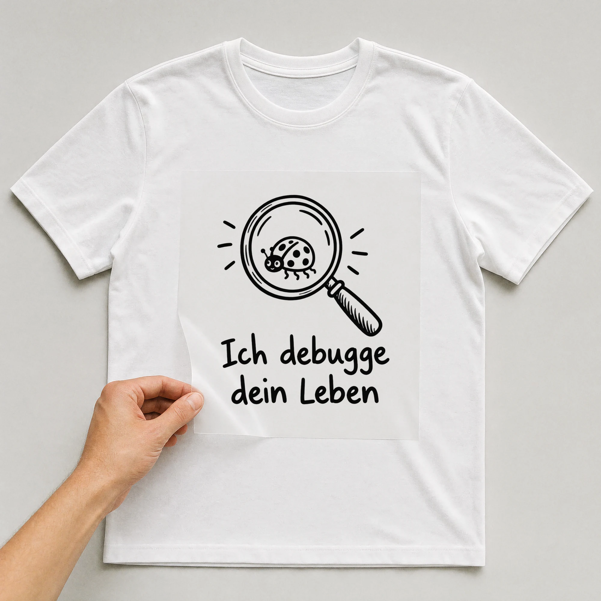 Bügelbild „Ich debugge dein Leben“ auf weißem T-Shirt, Folie wird aufgelegt