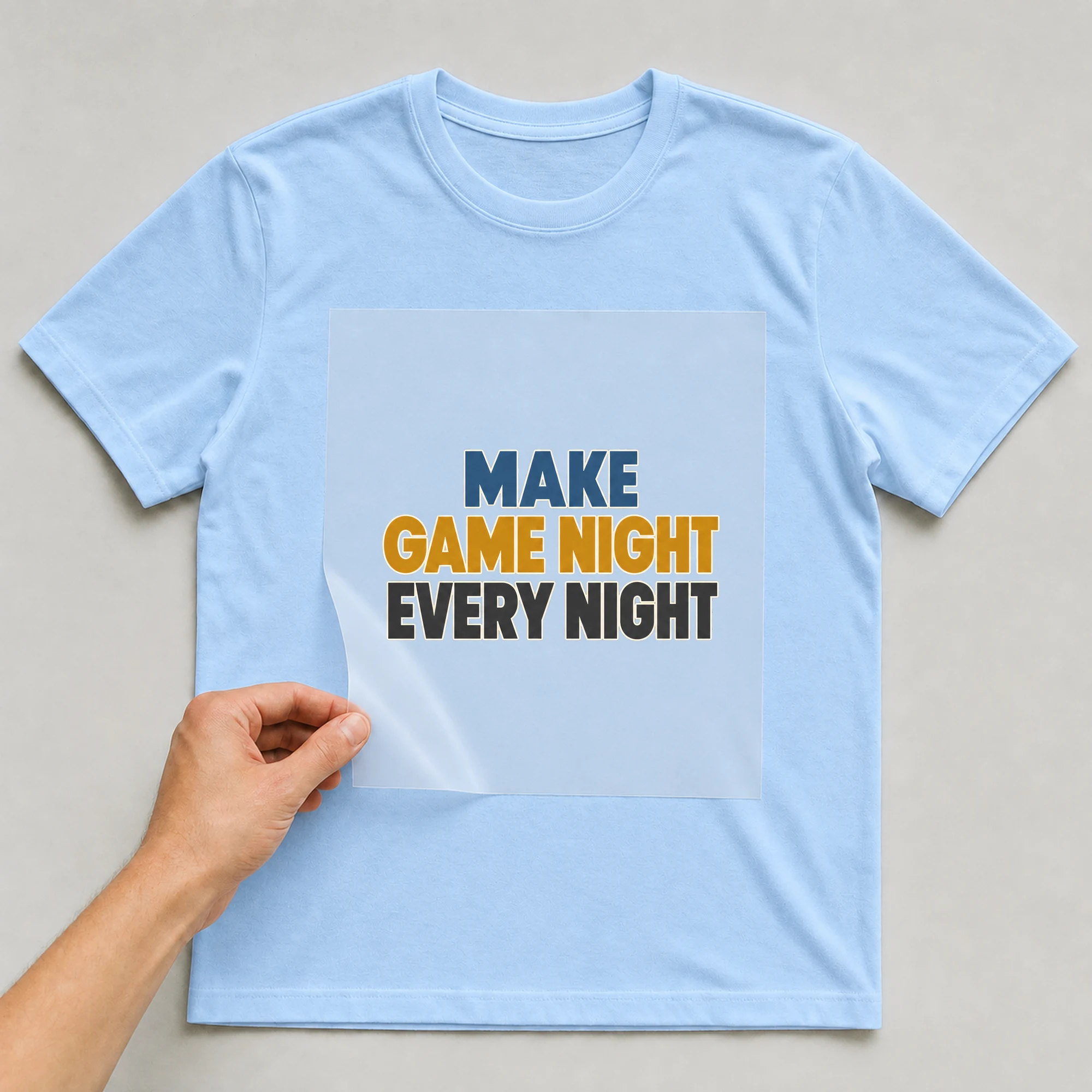 Bügelbild „MAKE GAME NIGHT EVERY NIGHT“ auf babyblauem T-Shirt, Folie wird aufgelegt