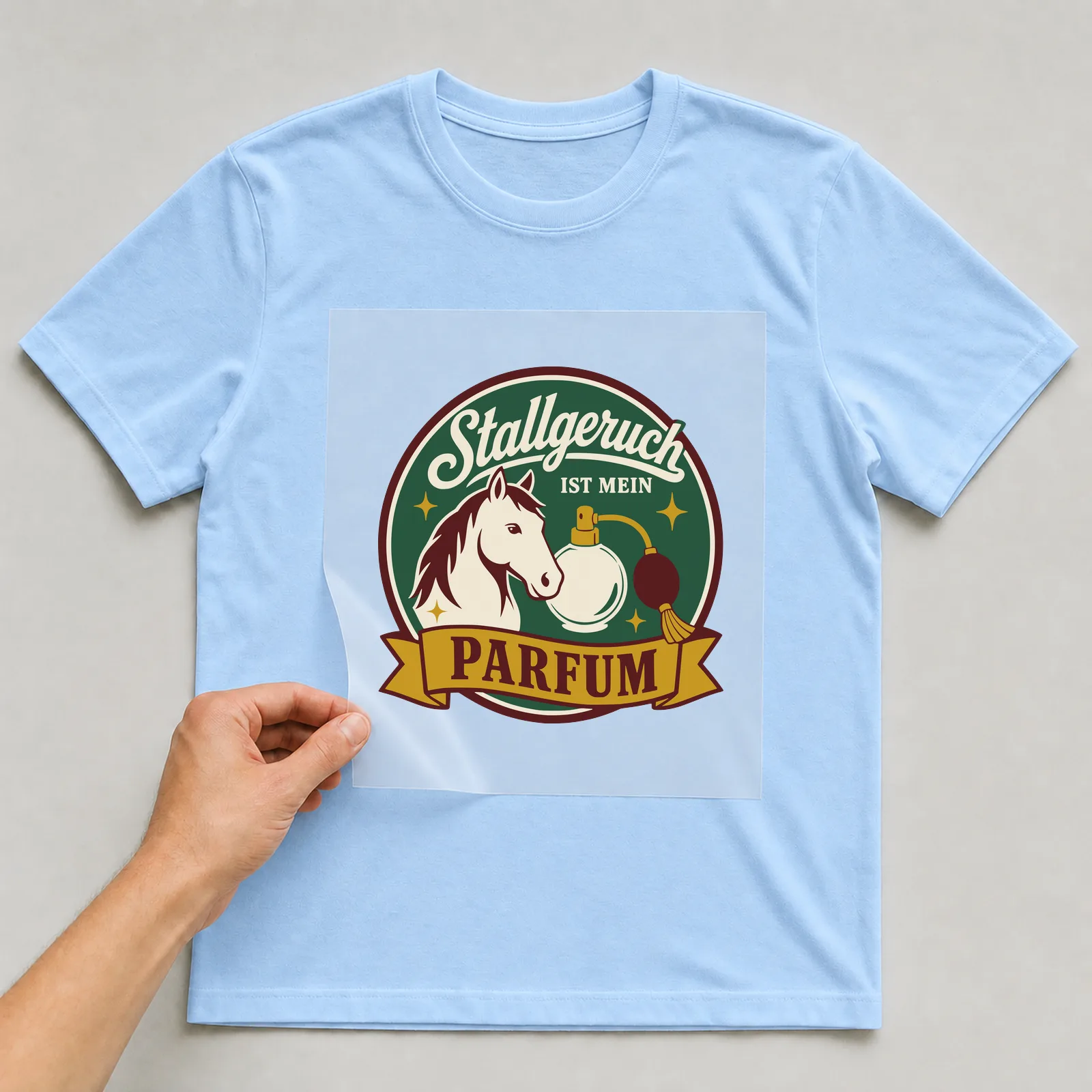 Bügelbild Stallgeruch ist mein Parfum auf hellblauem T-Shirt, Folie wird aufgelegt