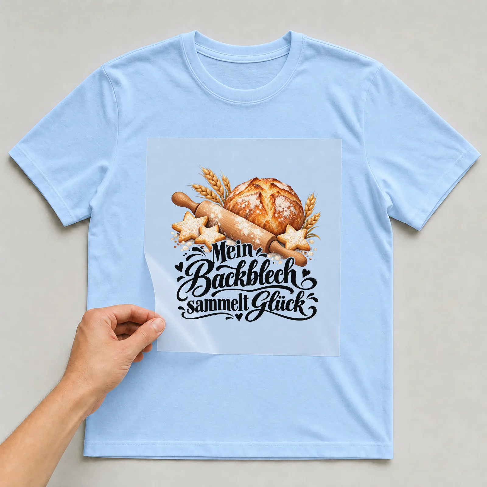 Bügelbild „Mein Backblech sammelt Glück“ auf hellblauem T-Shirt, Folie wird aufgelegt