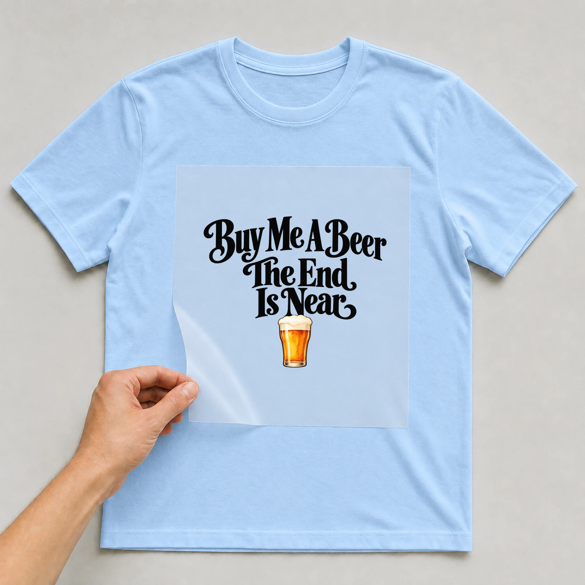 Bügelbild „Buy Me A Beer The End Is Near“ auf babyblauem T-Shirt, Folie wird aufgelegt