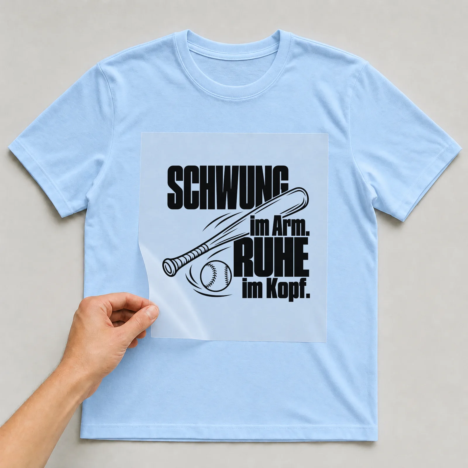 Bügelbild „Schwung im Arm. Ruhe im Kopf.“ auf hellblauem T-Shirt, Folie wird aufgelegt