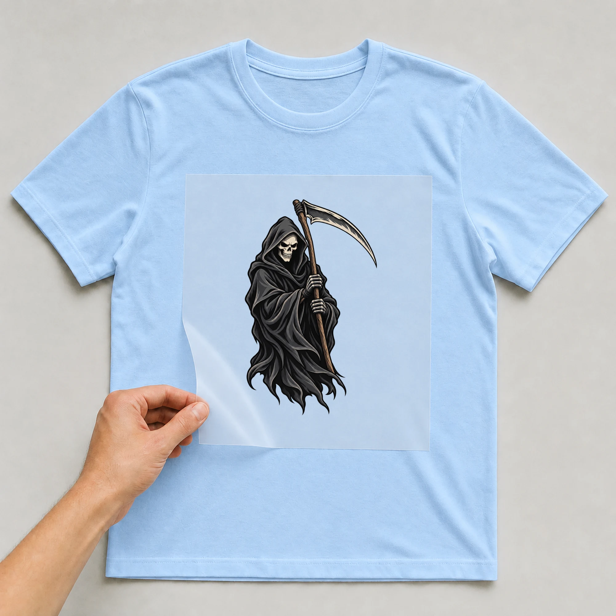 Bügelbild „Der Sensenmann“ auf babyblauem T-Shirt, Folie wird aufgelegt