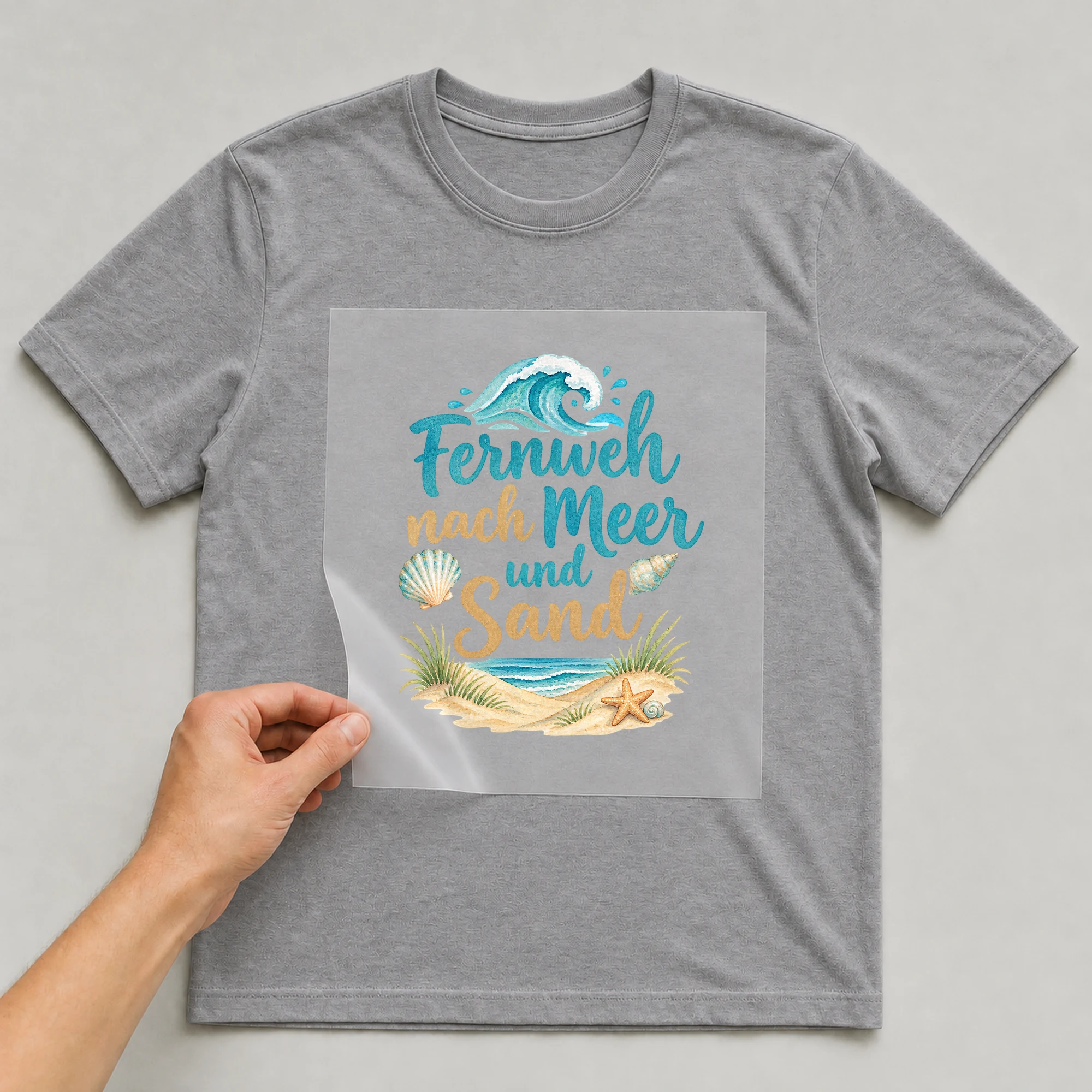 Bügelbild „Fernweh nach meer und sand“ auf grauem T-Shirt, Folie wird aufgelegt