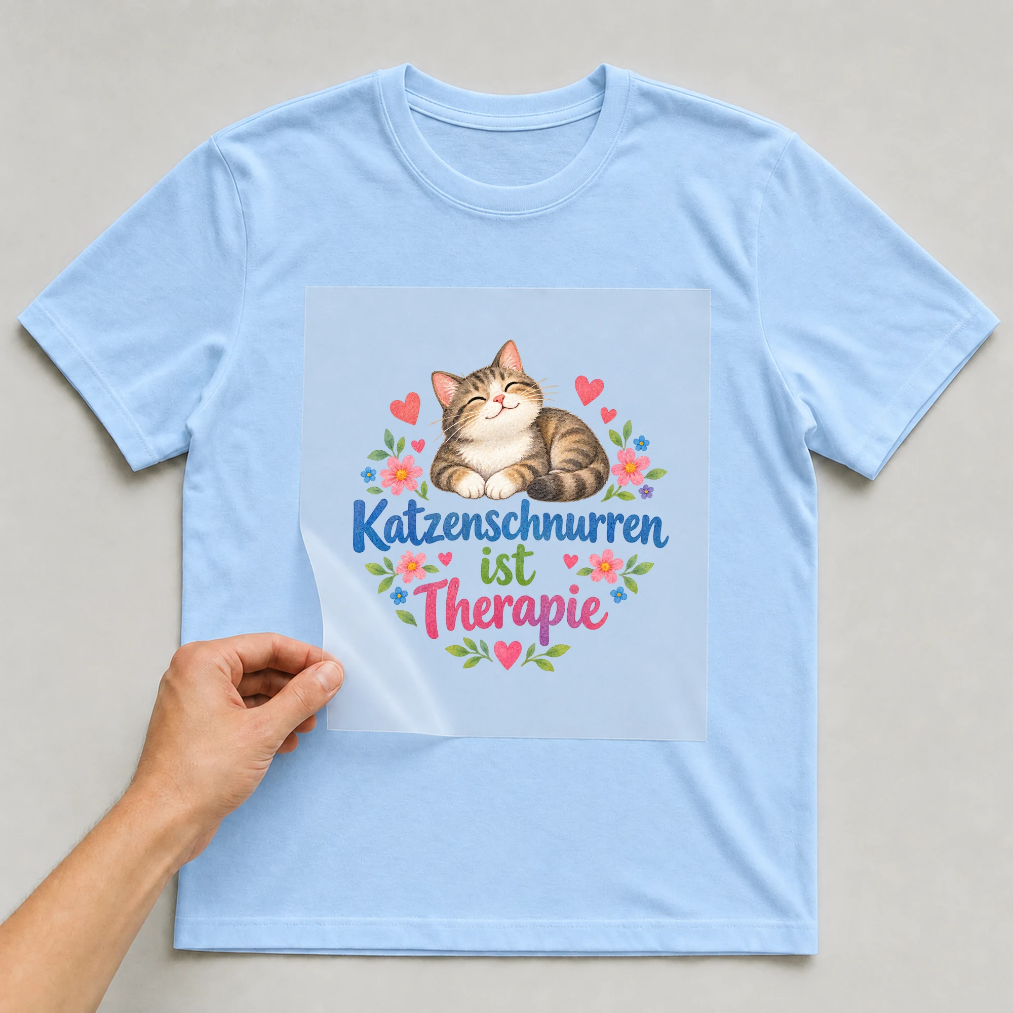 Bügelbild „Katzenschnurren ist Therapie“ auf babyblauem T-Shirt, Folie wird aufgelegt
