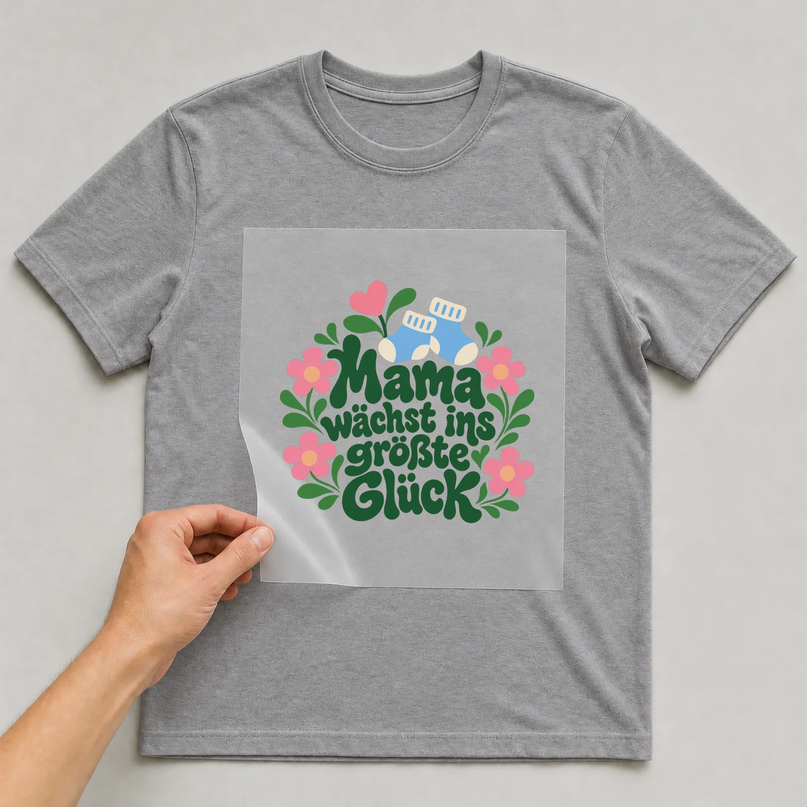 Bügelbild „Mama wächst ins größte Glück“ auf grauem T-Shirt, Folie wird aufgelegt