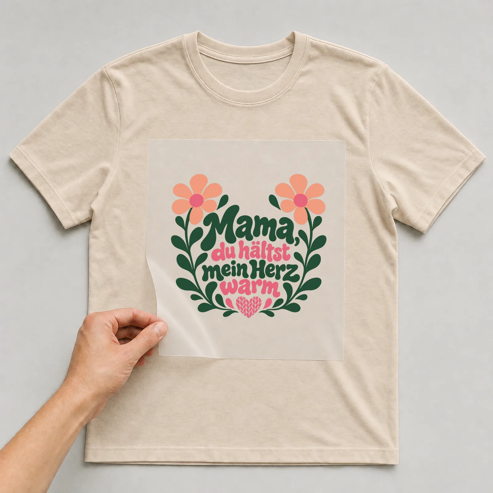 Bügelbild „Mama, du hältst mein Herz warm“ auf beigem T-Shirt, Folie wird aufgelegt