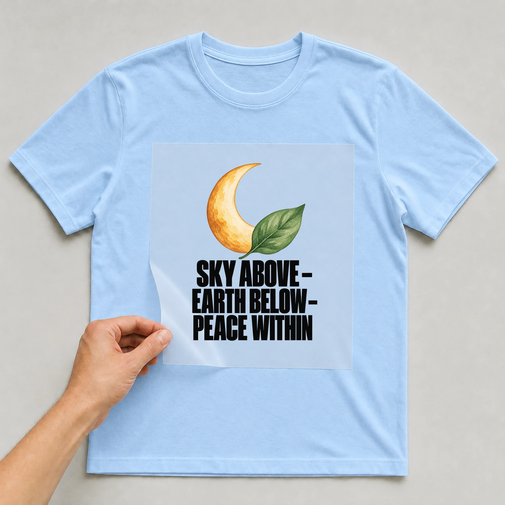 Bügelbild „Sky Above - Earth Below - Peace Within“ auf babyblauem T-Shirt, Folie wird aufgelegt