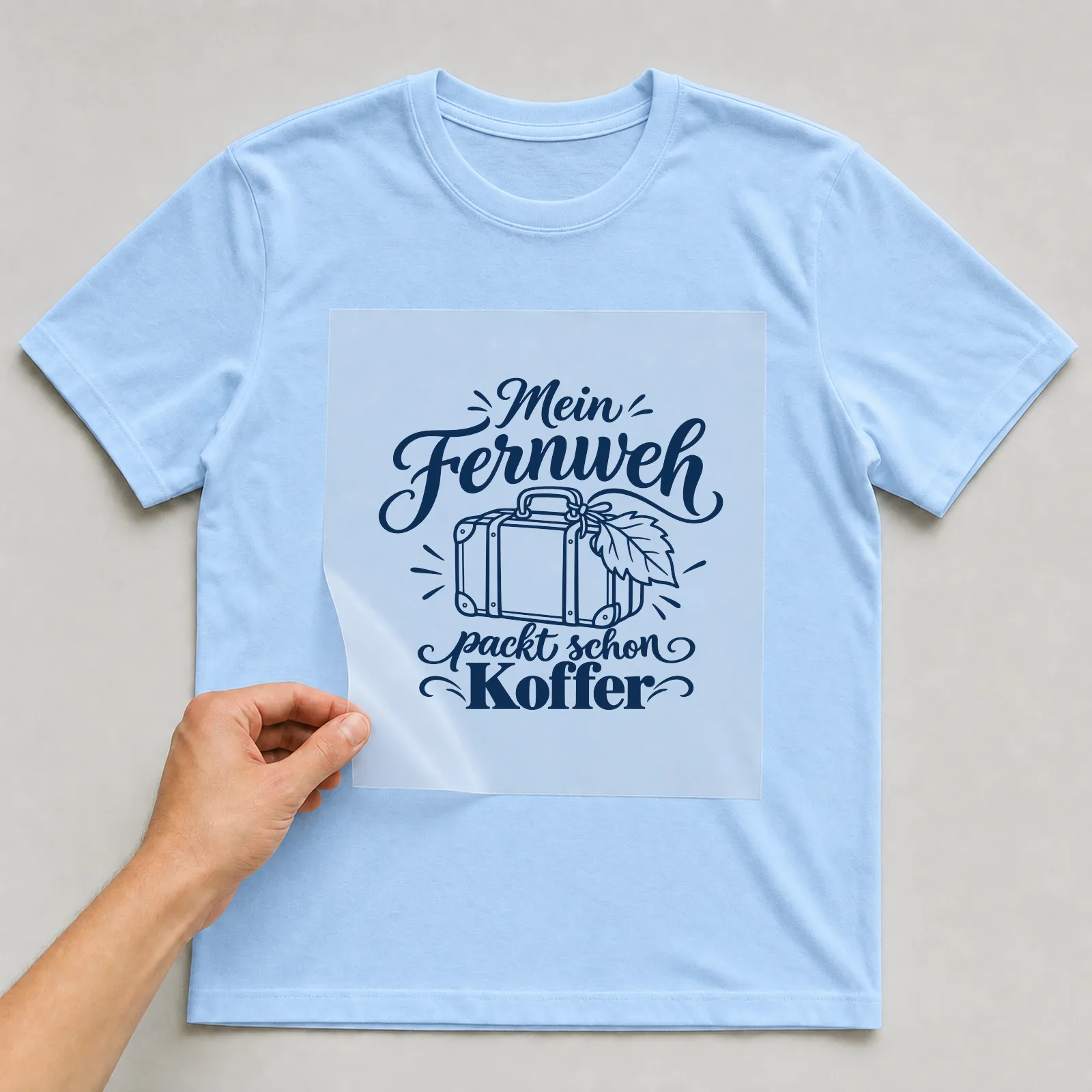 Bügelbild „Mein Fernweh packt schon Koffer“ auf hellblauem T-Shirt, Folie wird aufgelegt