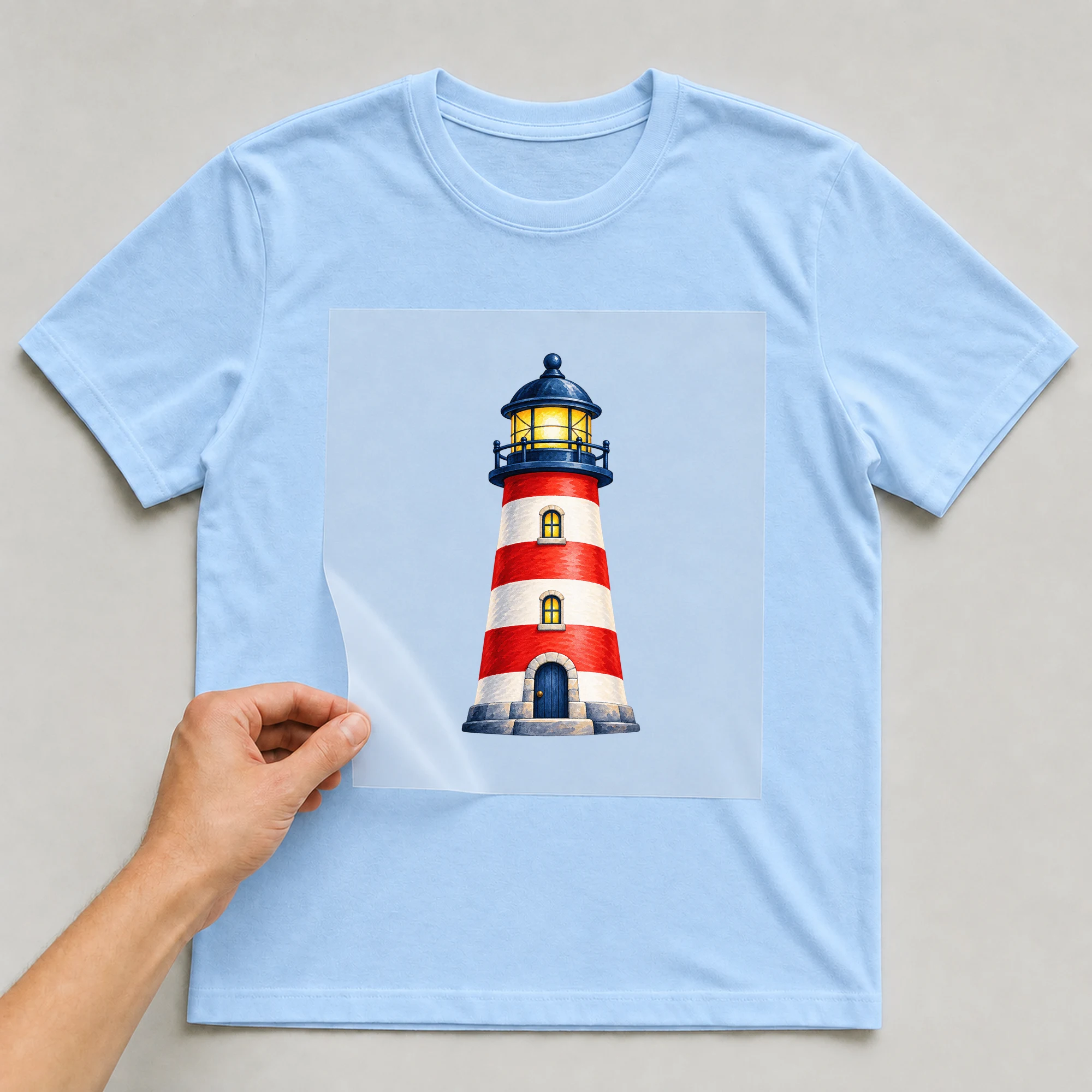 Bügelbild „Ostsee Leuchtturm“ auf babyblauem T-Shirt, Folie wird aufgelegt