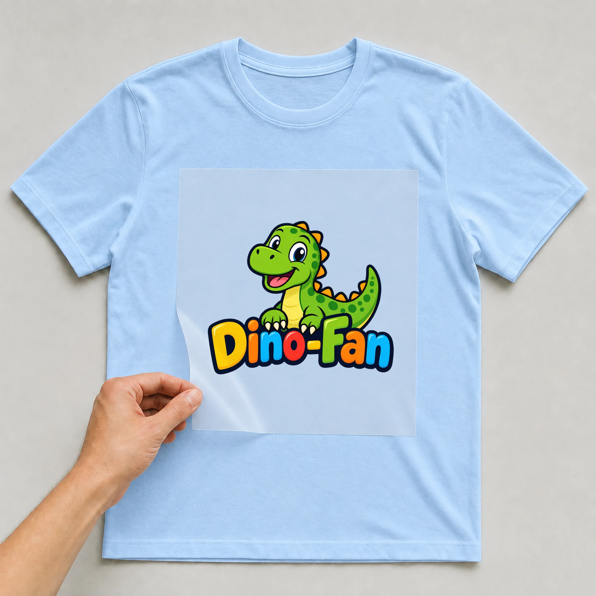 Bügelbild „Dino-Fan“ auf babyblauem T-Shirt, Folie wird aufgelegt