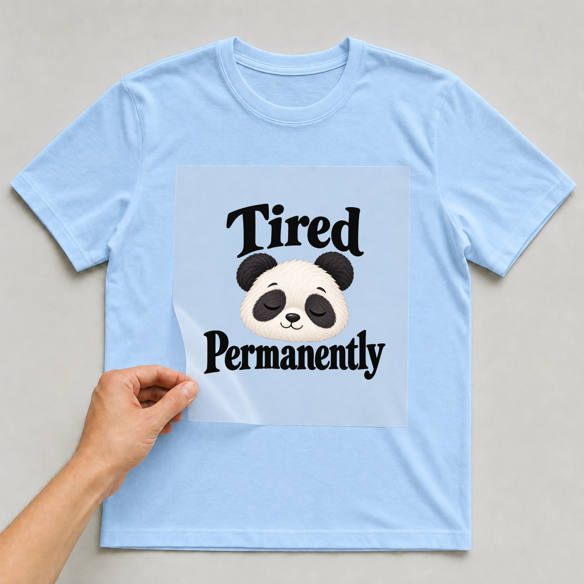 Bügelbild „Tired Permanently“ auf babyblauem T-Shirt, Folie wird aufgelegt