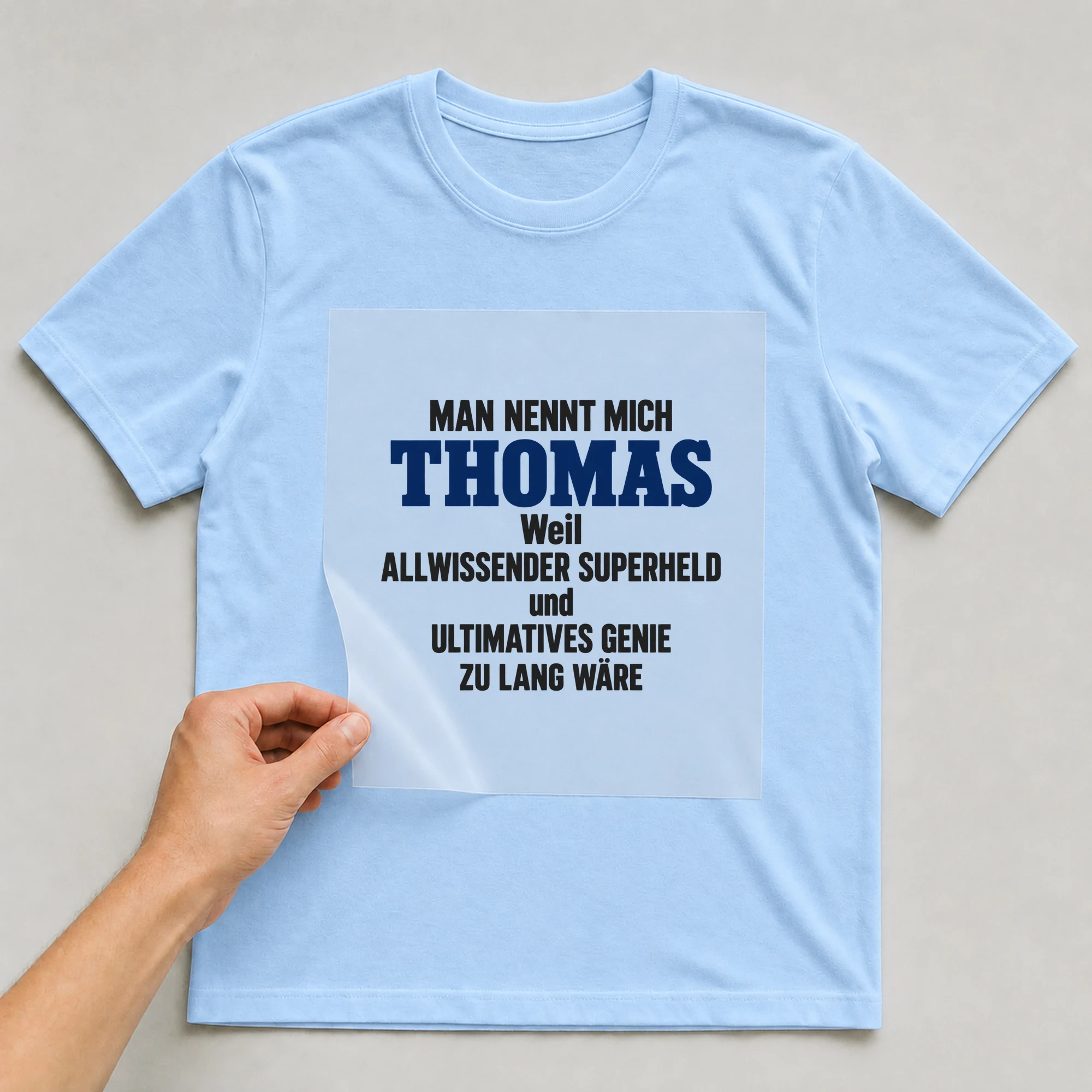 Bügelbild „Man nennt mich Thomas weil allwissender Superheld und ultimatives Genie zu“ auf babyblauem T-Shirt, Folie wird aufgelegt