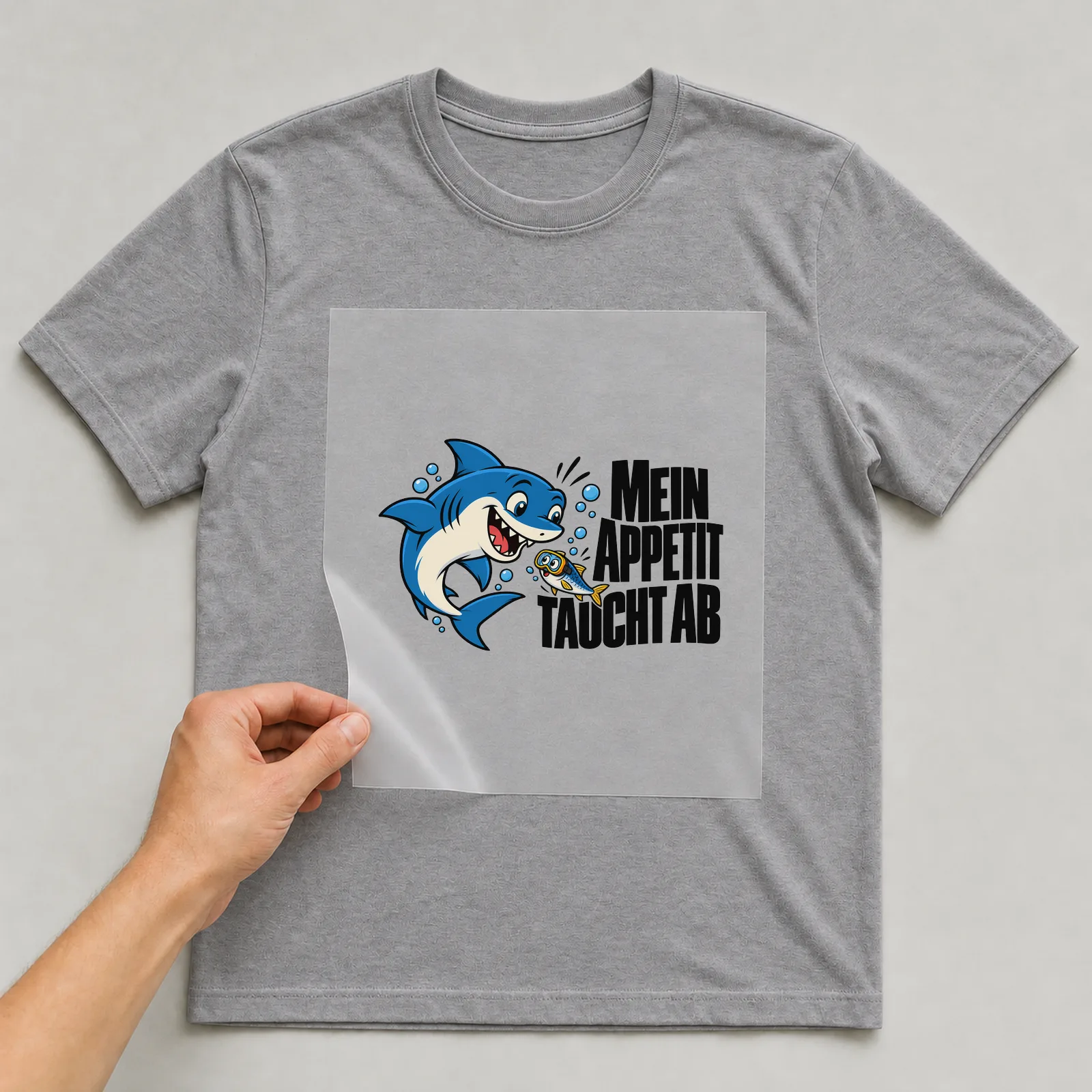 Bügelbild „Mein Appetit taucht ab“ auf grauem T-Shirt, Folie wird aufgelegt
