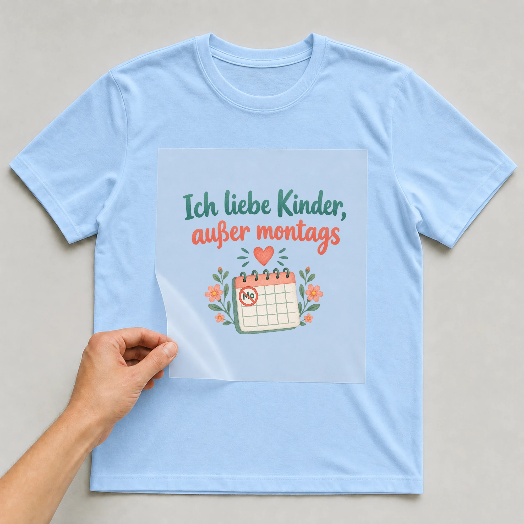 Bügelbild „Ich liebe Kinder, außer montags“ auf babyblauem T-Shirt, Folie wird aufgelegt