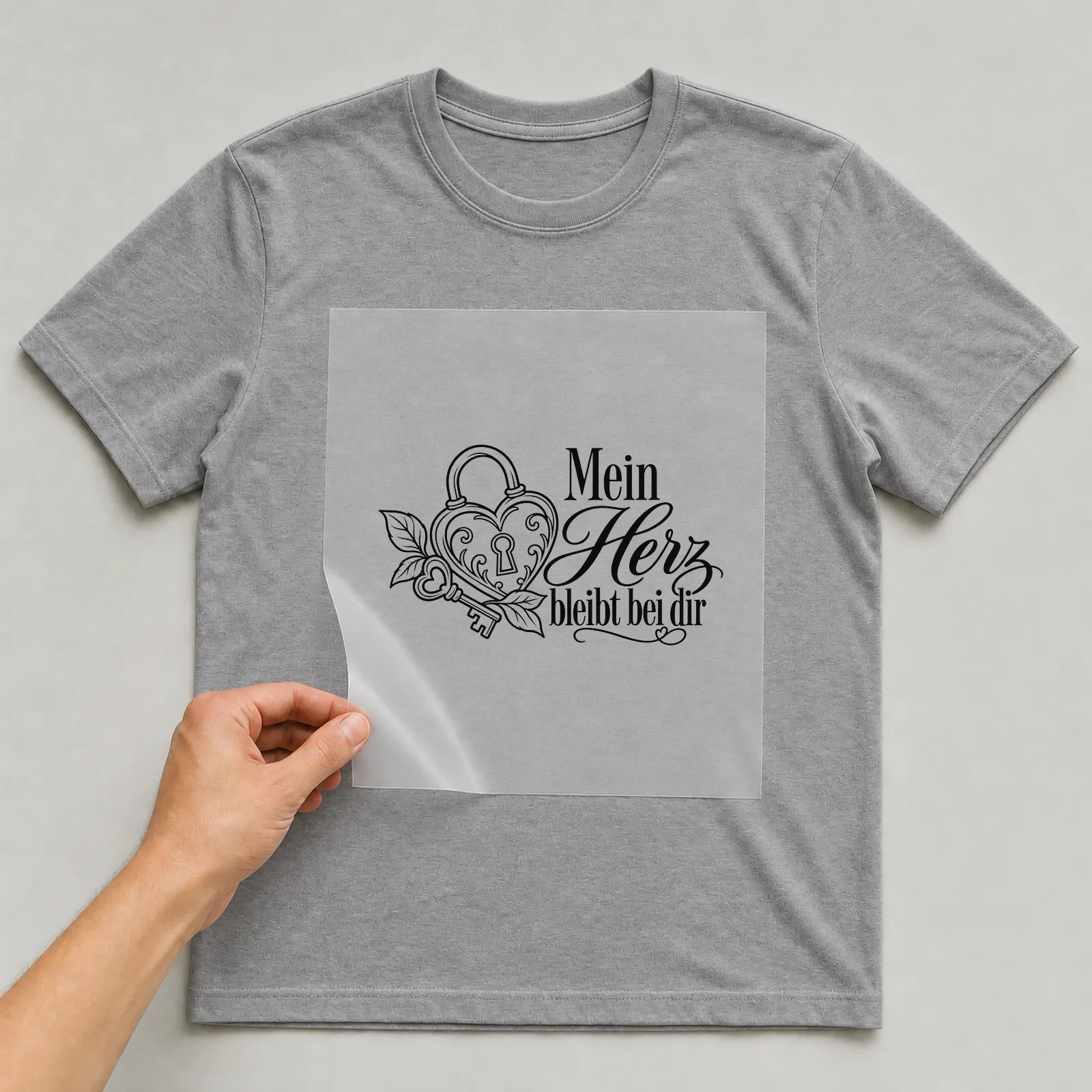 Bügelbild „Mein Herz bleibt bei dir“ auf grauem T-Shirt, Folie wird aufgelegt