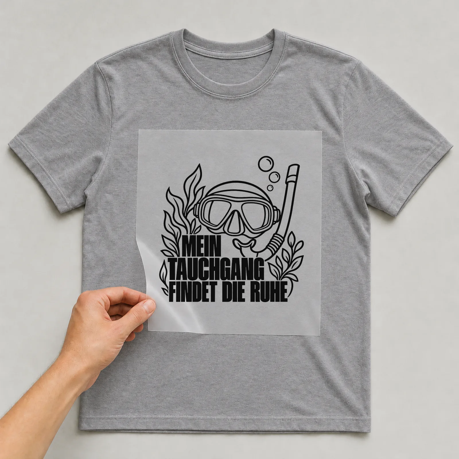 Bügelbild „Mein Tauchgang findet die Ruhe“ auf grauem T-Shirt, Folie wird aufgelegt