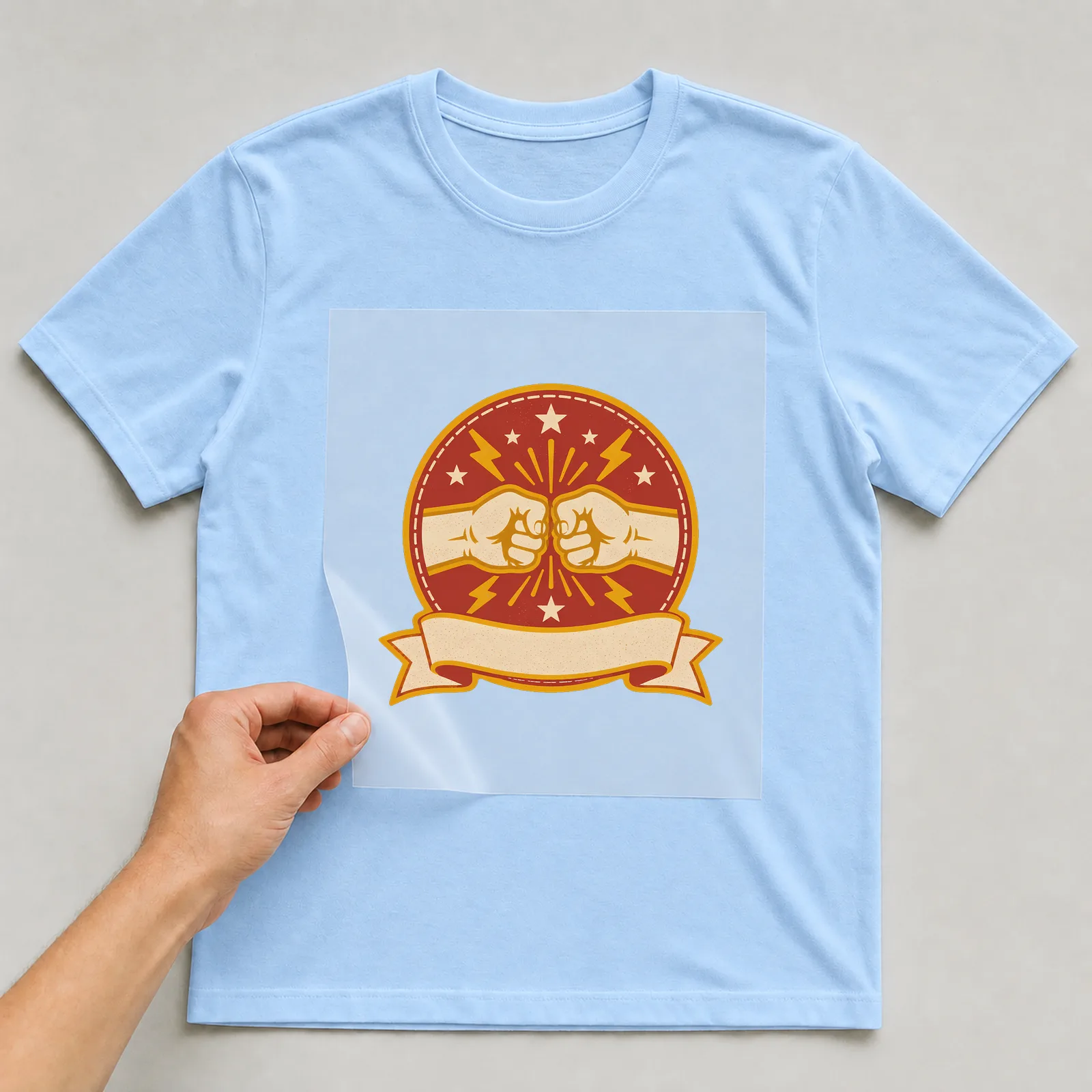 Bügelbild freundschaft faustgruss abzeichen auf hellblauem T-Shirt, Folie wird aufgelegt