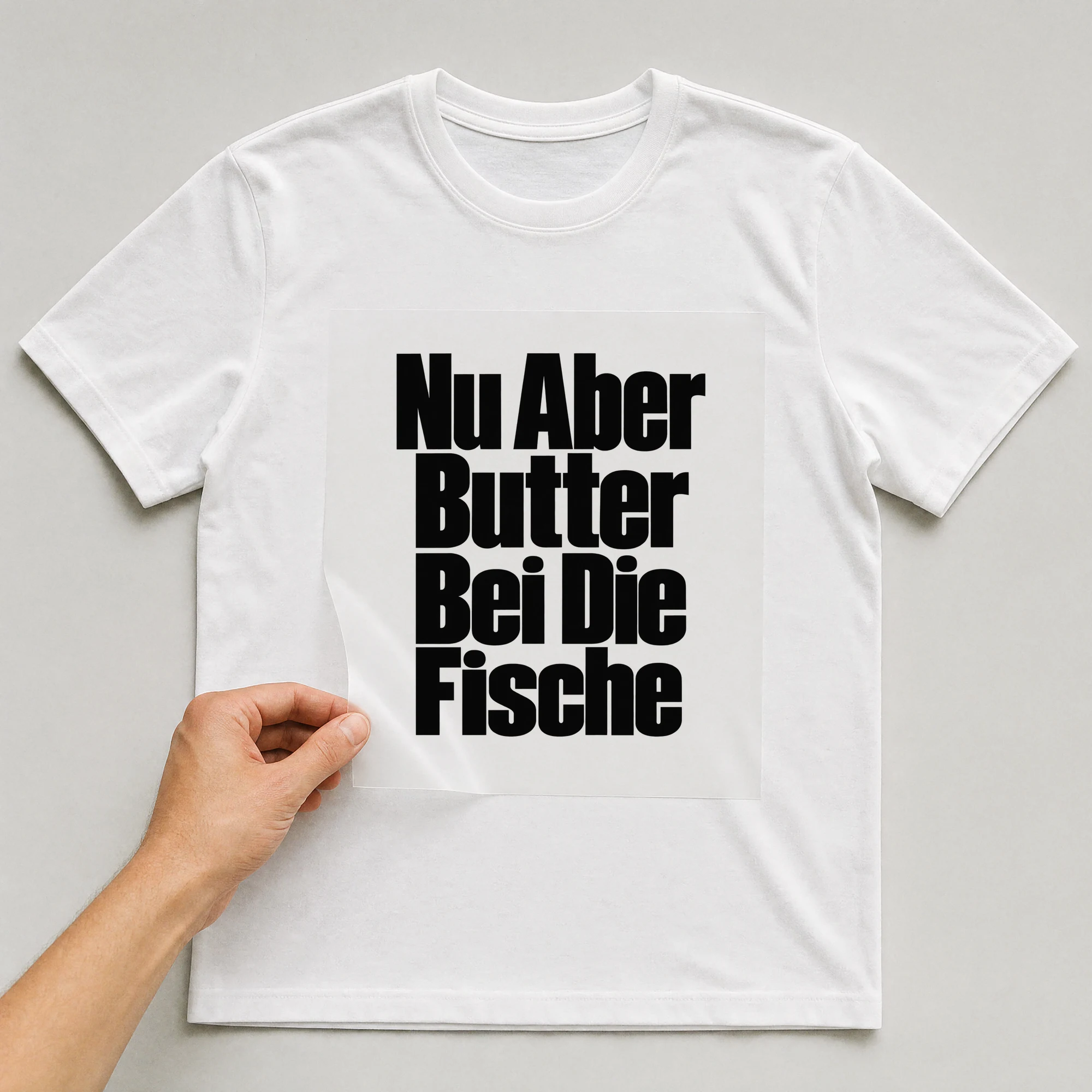 Bügelbild „Nu Aber Butter Bei Die Fische“ auf weißem T-Shirt, Folie wird aufgelegt