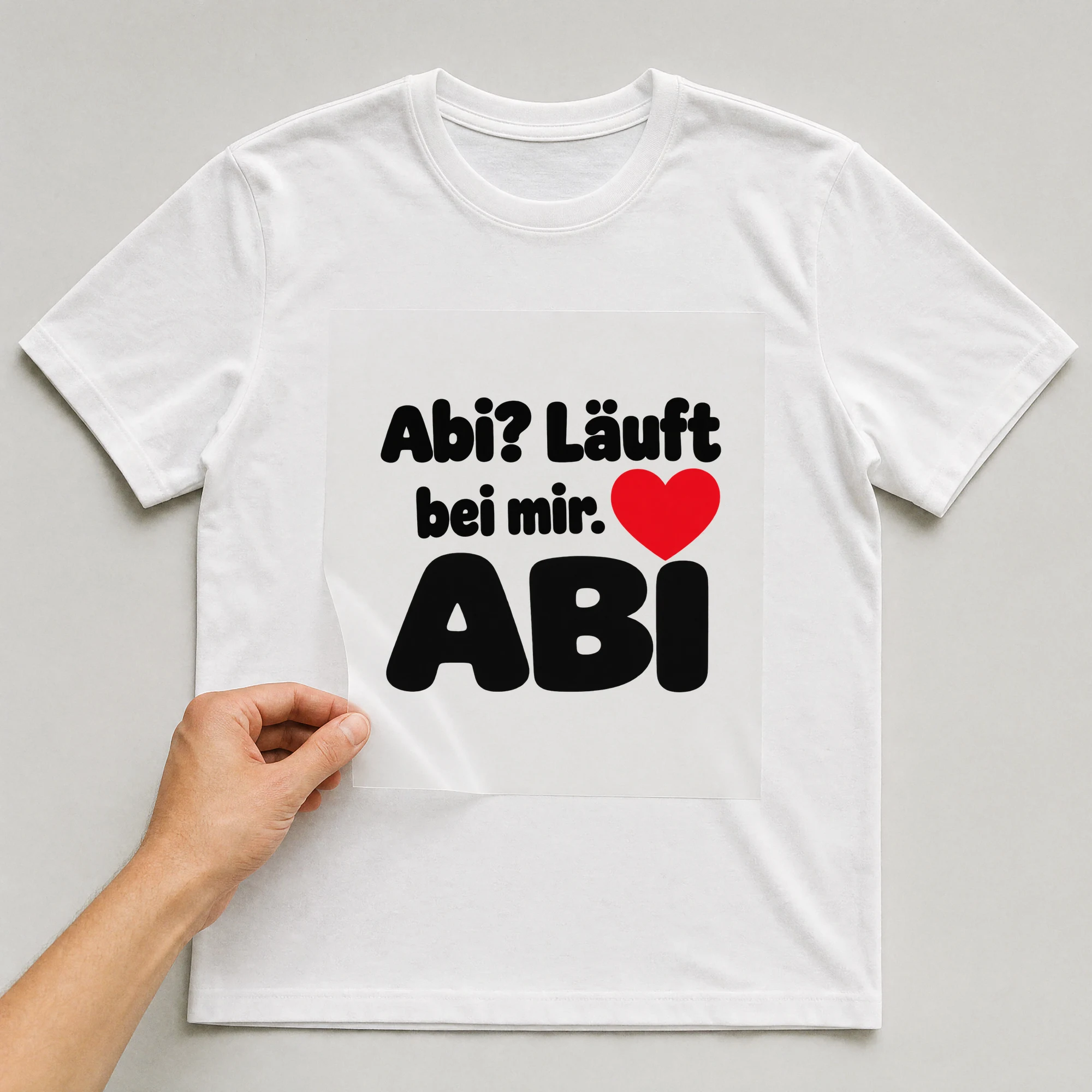 Bügelbild „Abi? Läuft bei mir.“ auf weißem T-Shirt, Folie wird aufgelegt
