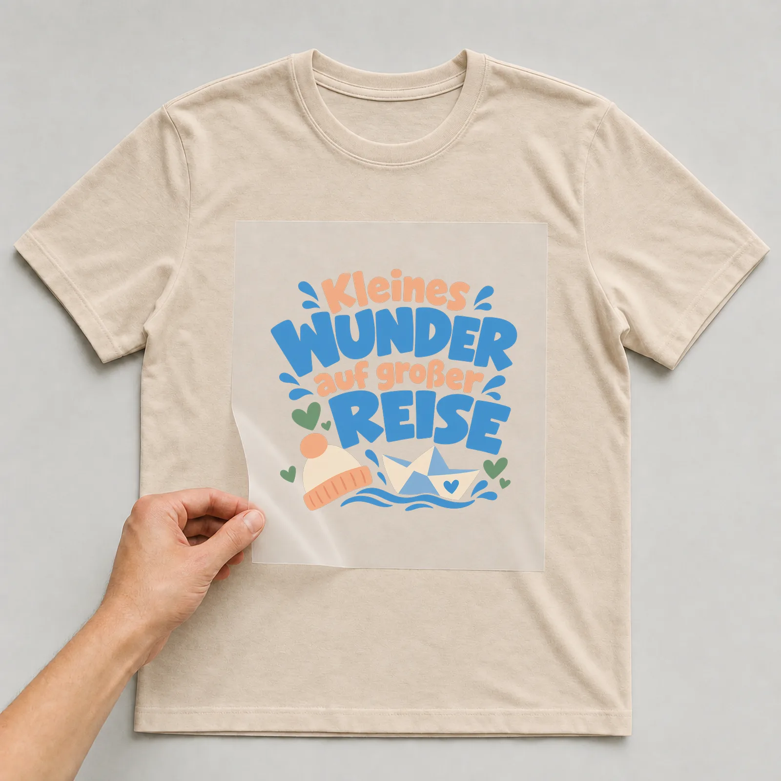 Bügelbild „Kleines Wunder auf großer Reise“ auf beigem T-Shirt, Folie wird aufgelegt