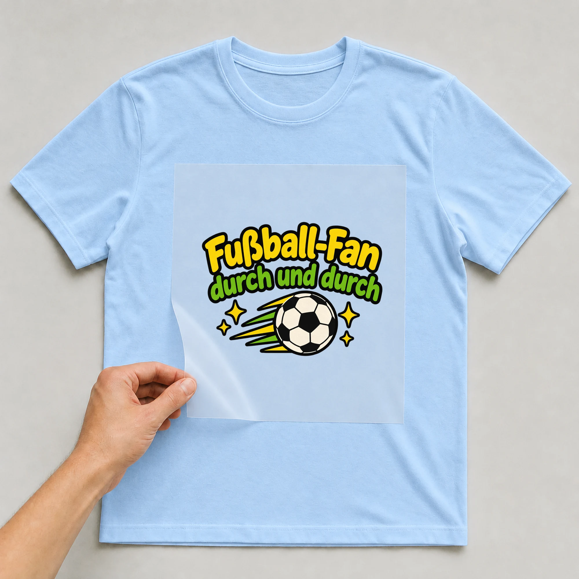 Bügelbild „Fußball-Fan durch und durch“ auf babyblauem T-Shirt, Folie wird aufgelegt