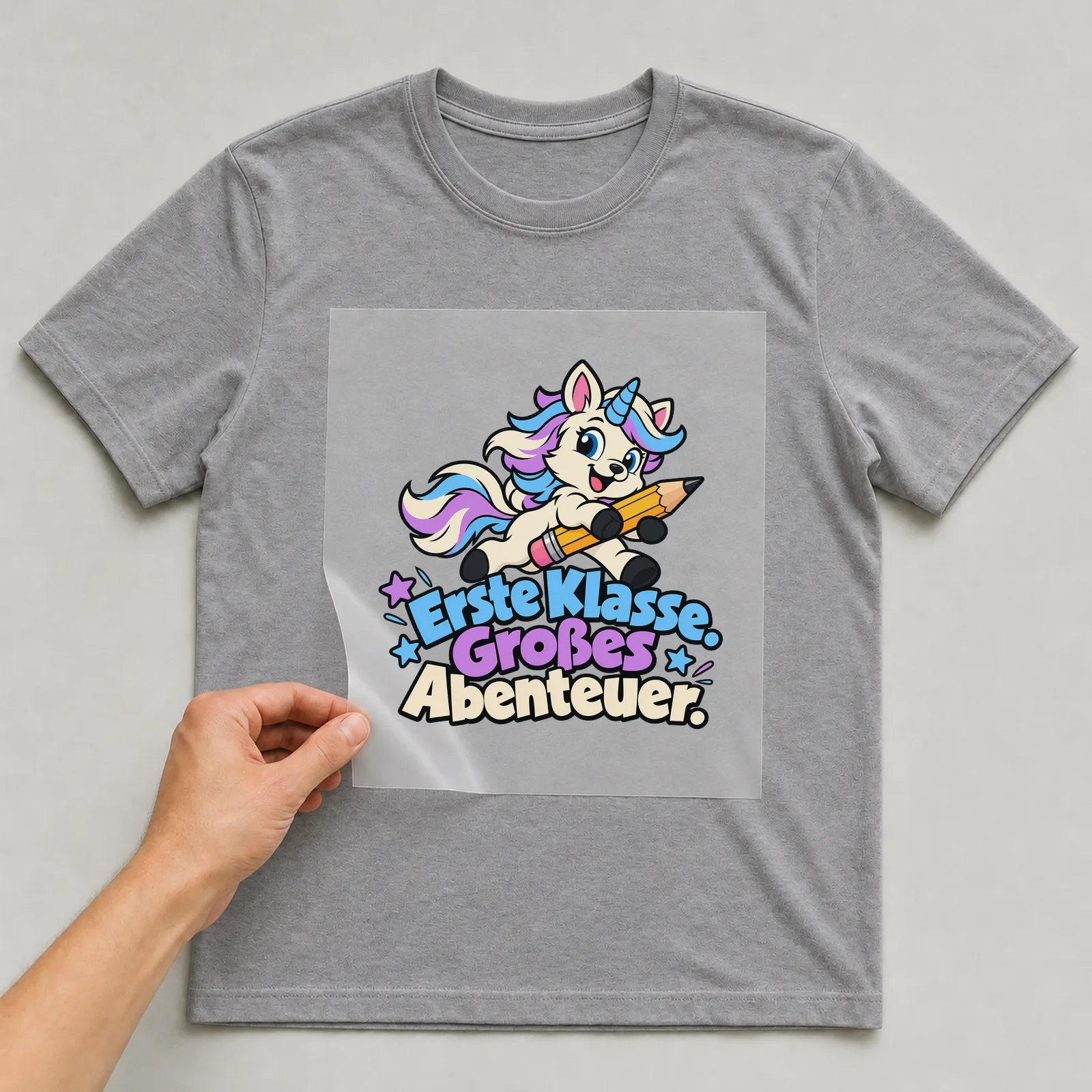 Bügelbild „Erste Klasse. Großes Abenteuer.“ auf grauem T-Shirt, Folie wird aufgelegt