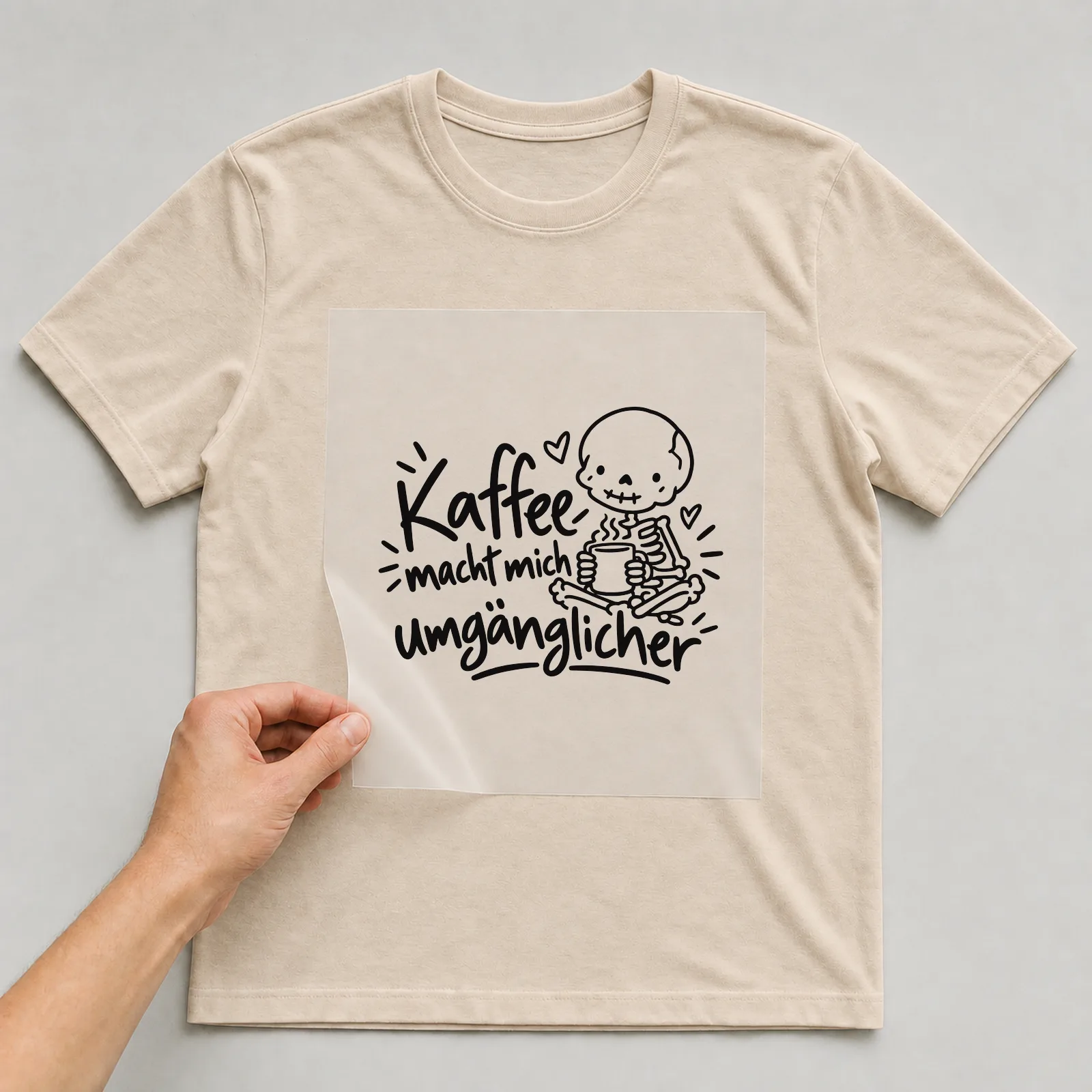 Bügelbild „Kaffee macht mich umgänglicher“ auf beigem T-Shirt, Folie wird aufgelegt