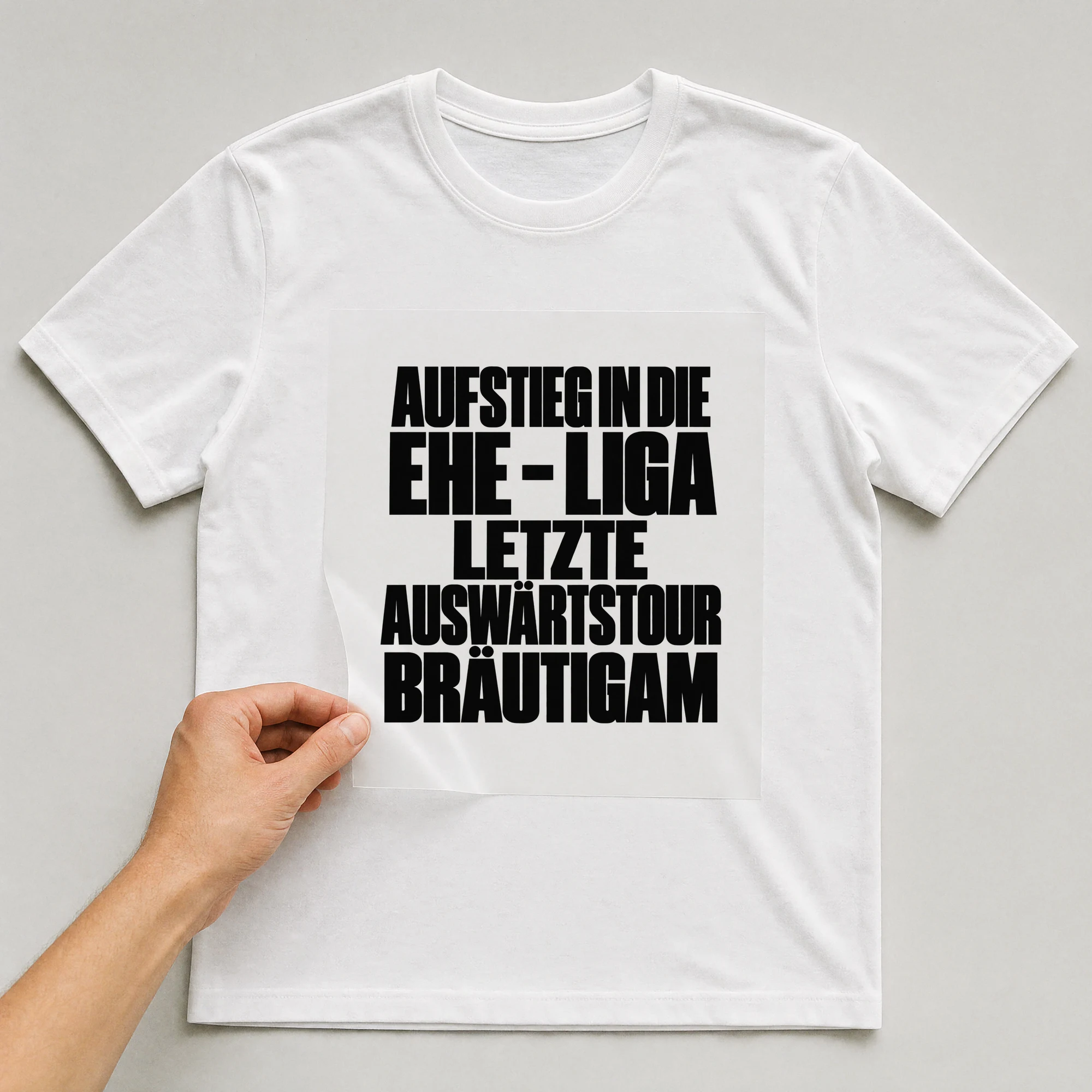 Bügelbild „Aufstieg in die Ehe - Liga letzte Auswärtstour Bräutigam“ auf weißem T-Shirt, Folie wird aufgelegt