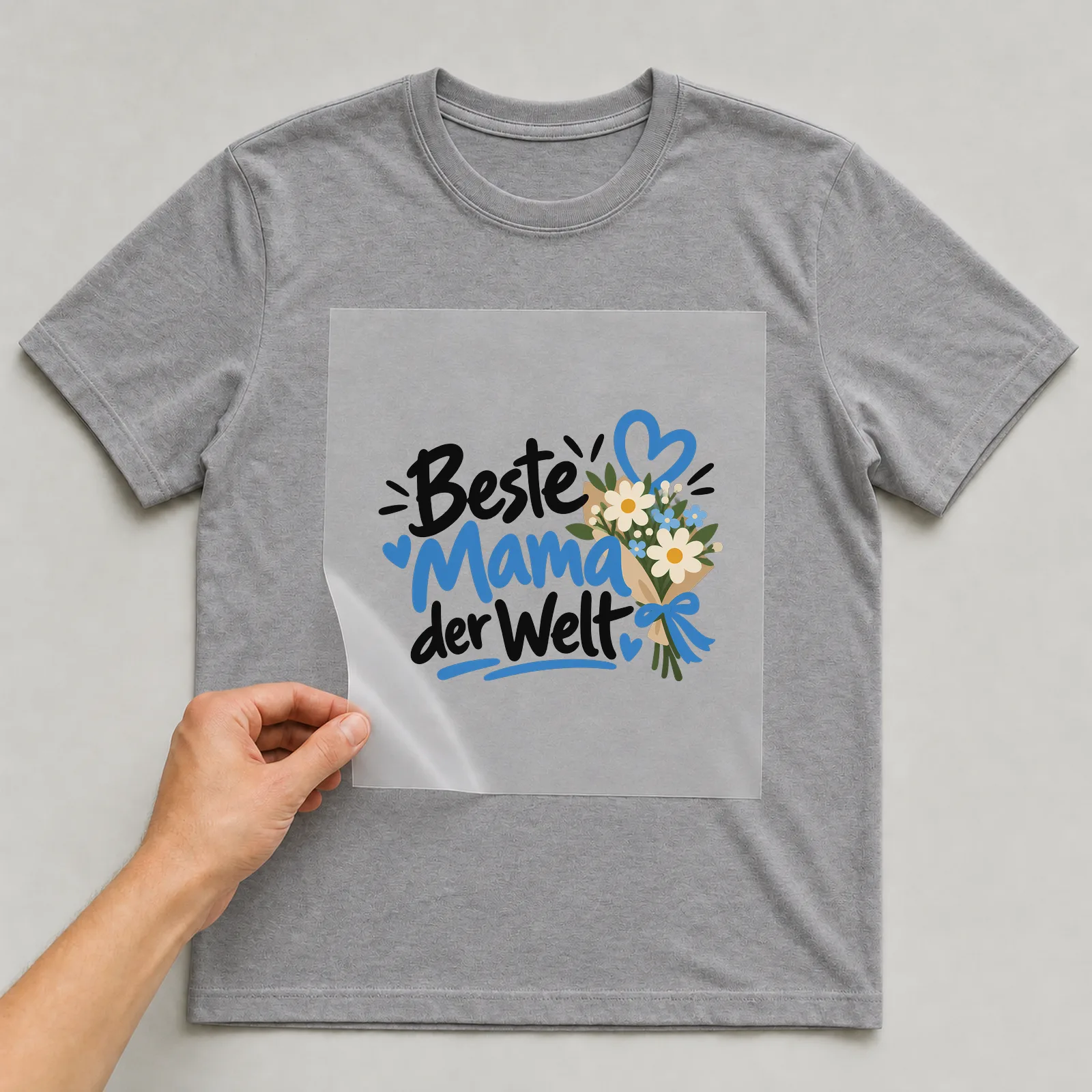 Bügelbild „Beste Mama der Welt“ (organischen Formen) auf grauem T-Shirt, Folie wird aufgelegt