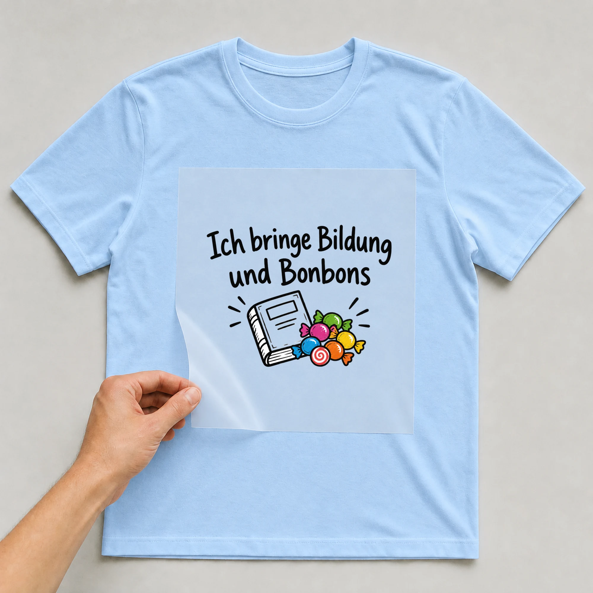 Bügelbild „Ich bringe Bildung und Bonbons“ auf babyblauem T-Shirt, Folie wird aufgelegt
