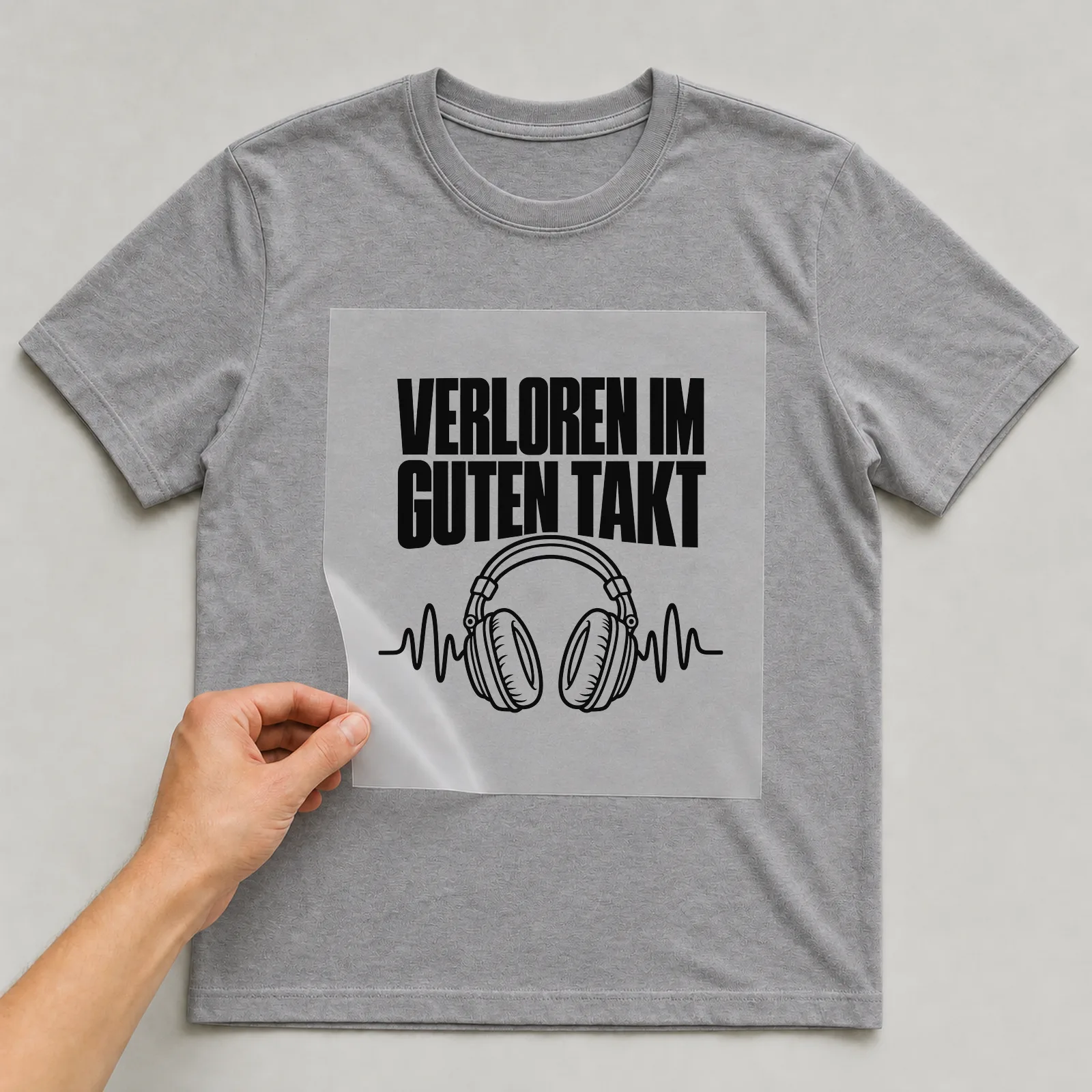Bügelbild „Verloren im guten Takt“ auf grauem T-Shirt, Folie wird aufgelegt