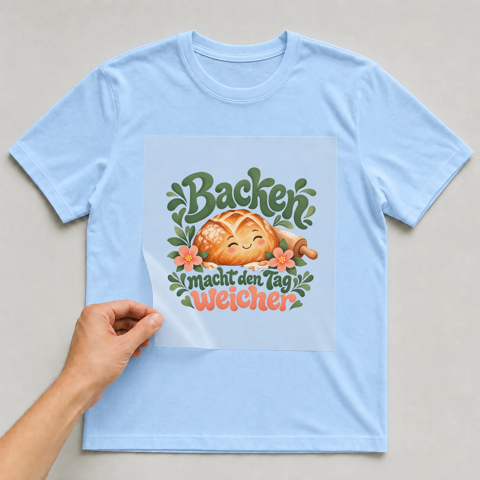Bügelbild „Backen macht den Tag weicher“ auf hellblauem T-Shirt, Folie wird aufgelegt