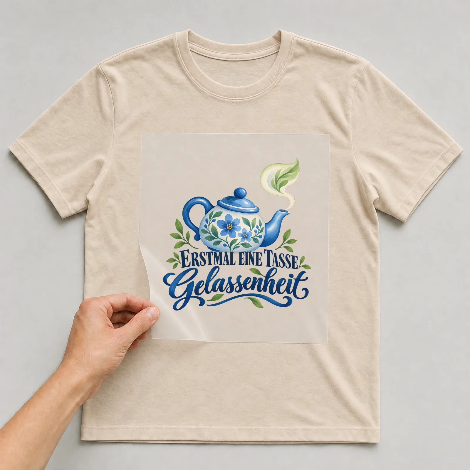 Bügelbild „Erstmal eine Tasse Gelassenheit“ auf beigem T-Shirt, Folie wird aufgelegt